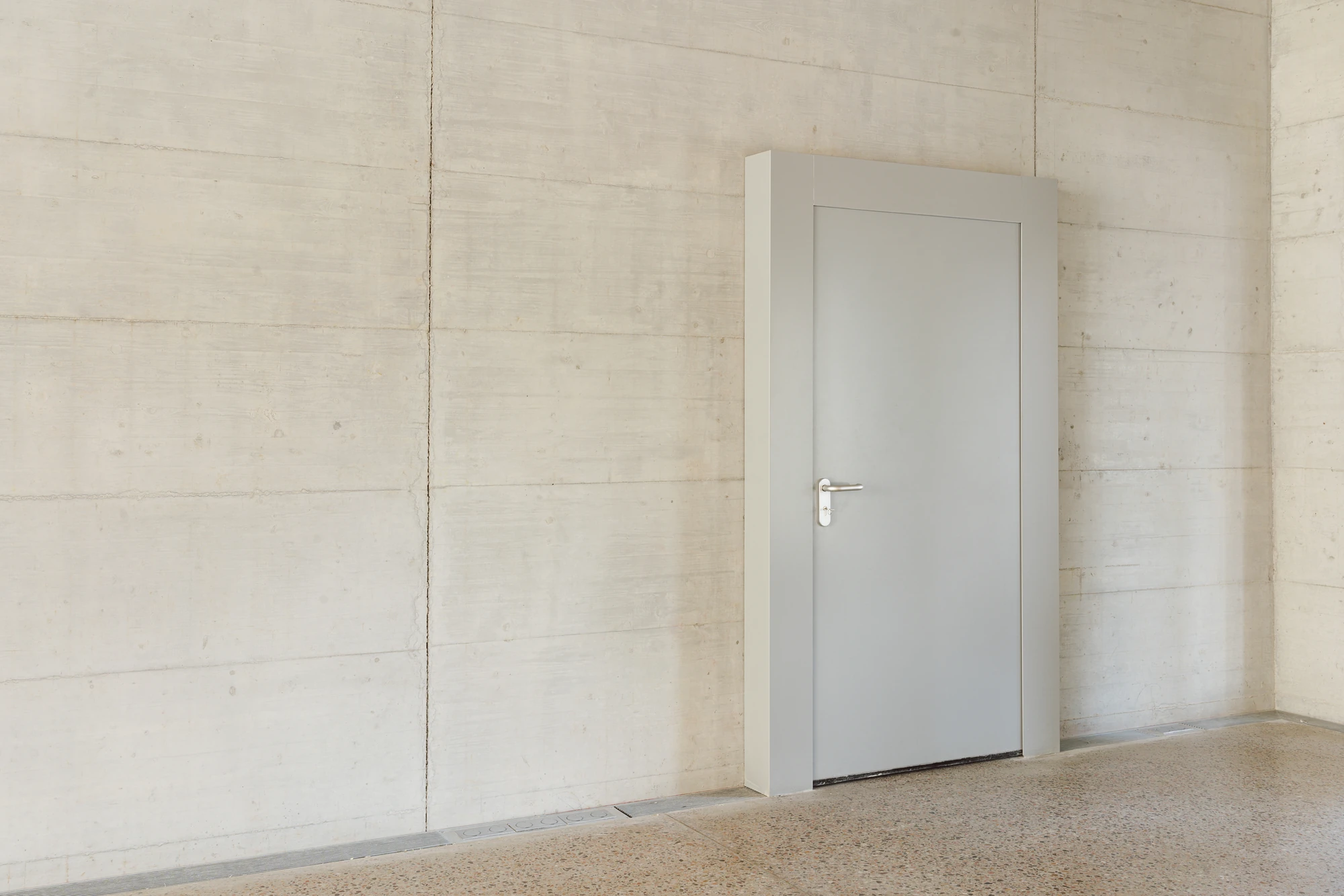 Biot Municipal Building Extension by Atelier EGR, photographed by Giaime Meloni — Interior corner of board-marked concrete with a flush grey door and a drainage channel set into the terrazzo.