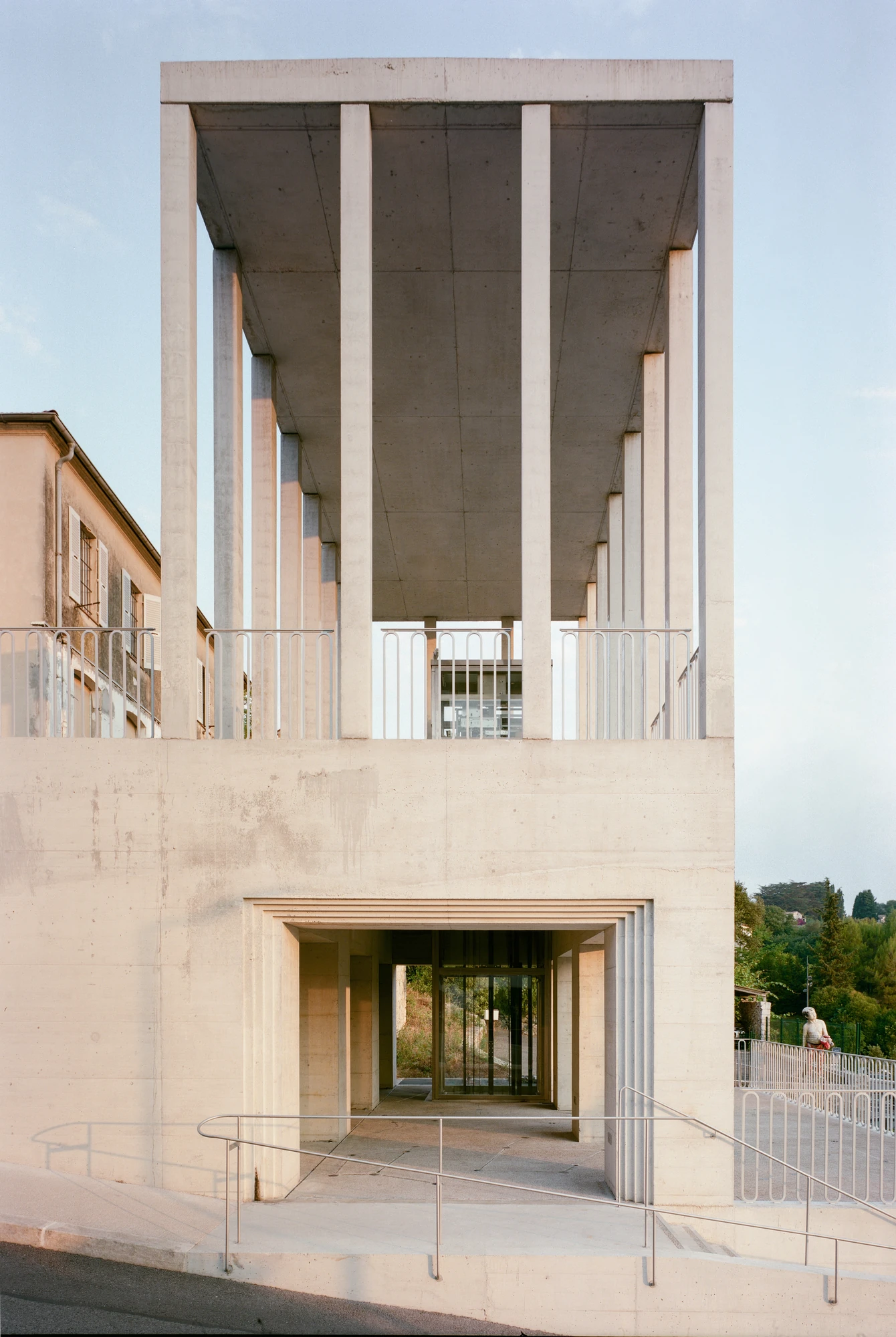Biot Municipal Building Extension by Atelier EGR, photographed by Giaime Meloni — The entrance bay framed by a stepped concrete reveal, with metal handrails running across the ramp in front of it.