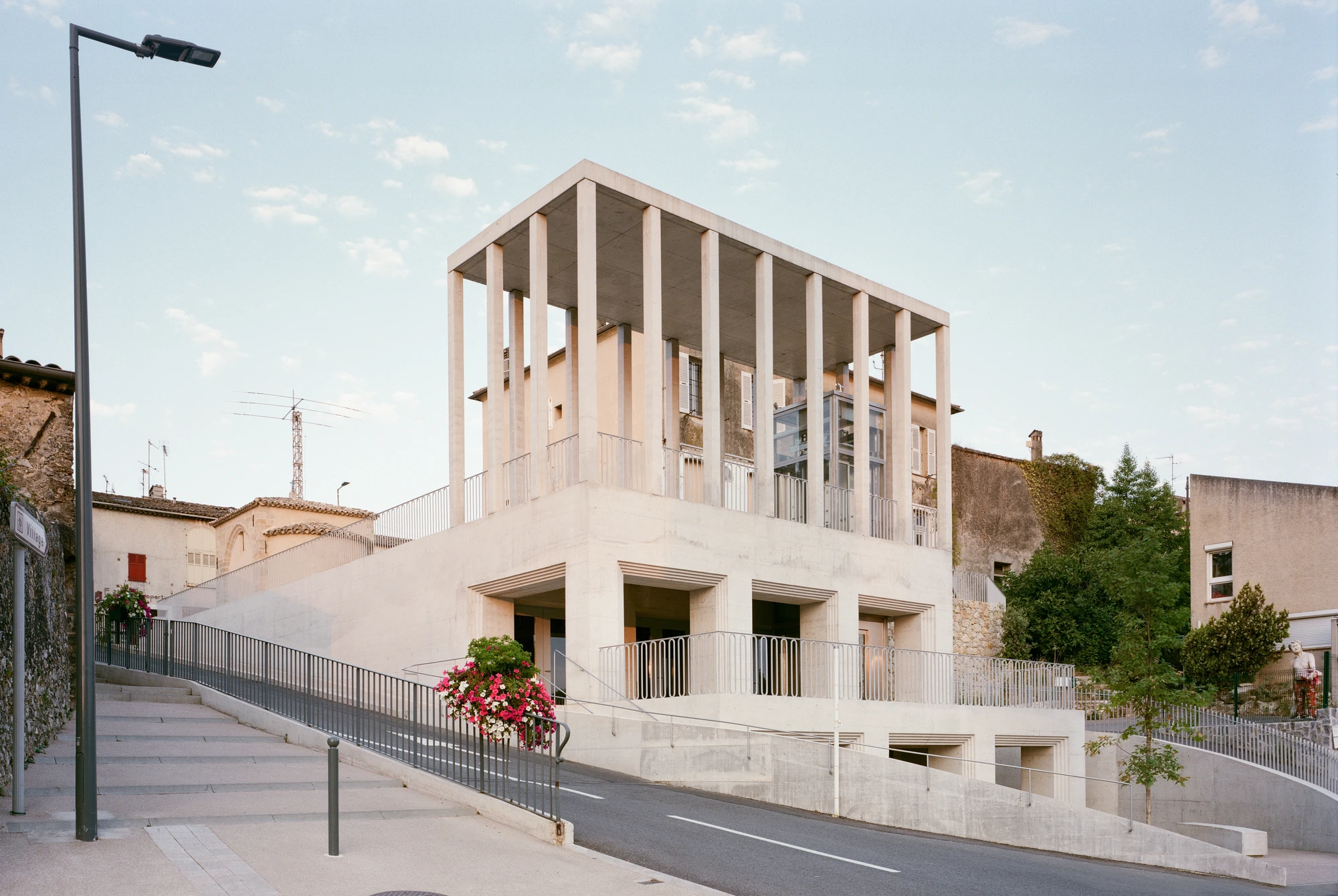 Biot Municipal Building Extension by Atelier EGR, photographed by Giaime Meloni — Street-corner view of the pale concrete volume, its columned upper level standing above older rendered houses on the hillside.