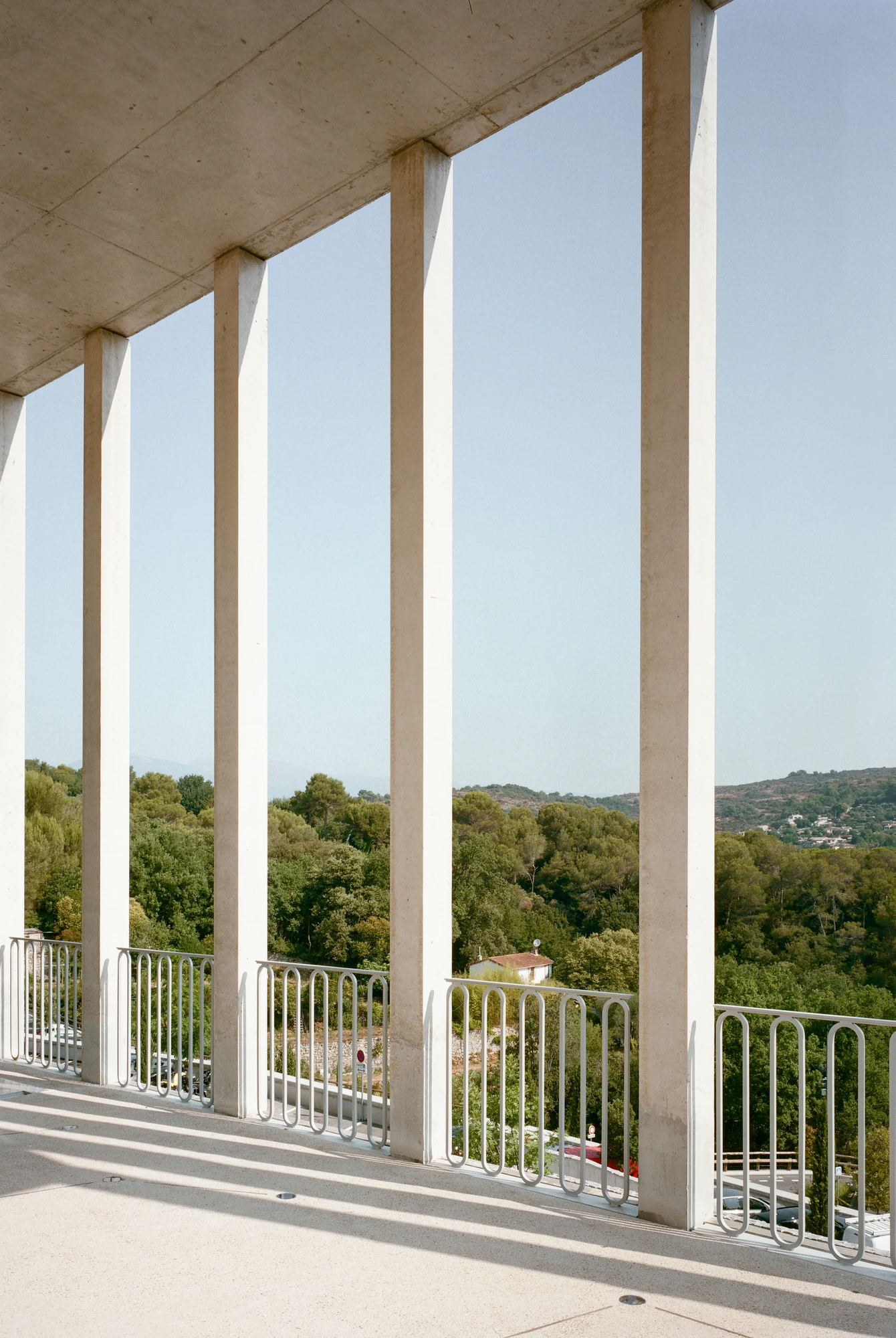 Biot Municipal Building Extension by Atelier EGR, photographed by Giaime Meloni — Looking between the columns from the covered terrace across the wooded valley and the ridge beyond.