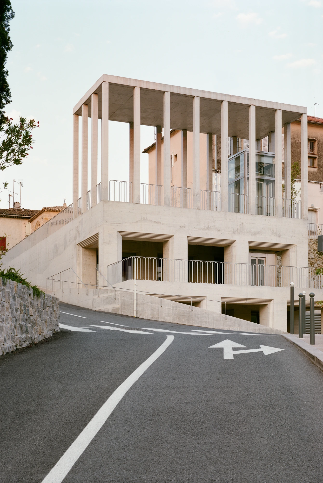 Biot Municipal Building Extension by Atelier EGR, photographed by Giaime Meloni — Seen from the road below, the terrace and columns rising over deep openings, with the glazed lift at the right.