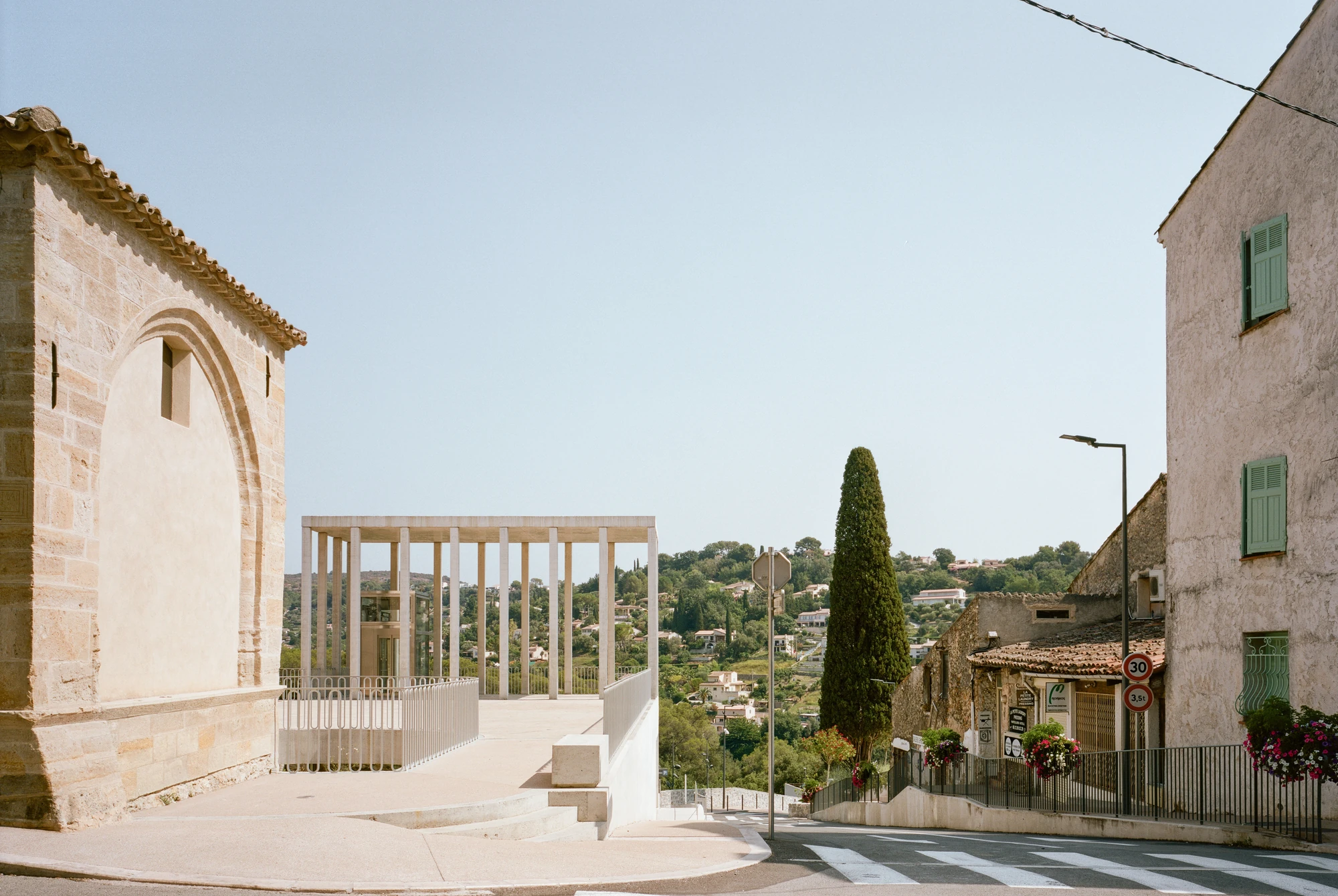 Biot Municipal Building Extension by Atelier EGR, photographed by Giaime Meloni — The stone gable of the Saint-Roch chapel in the foreground, with the columned belvedere and the valley behind it.