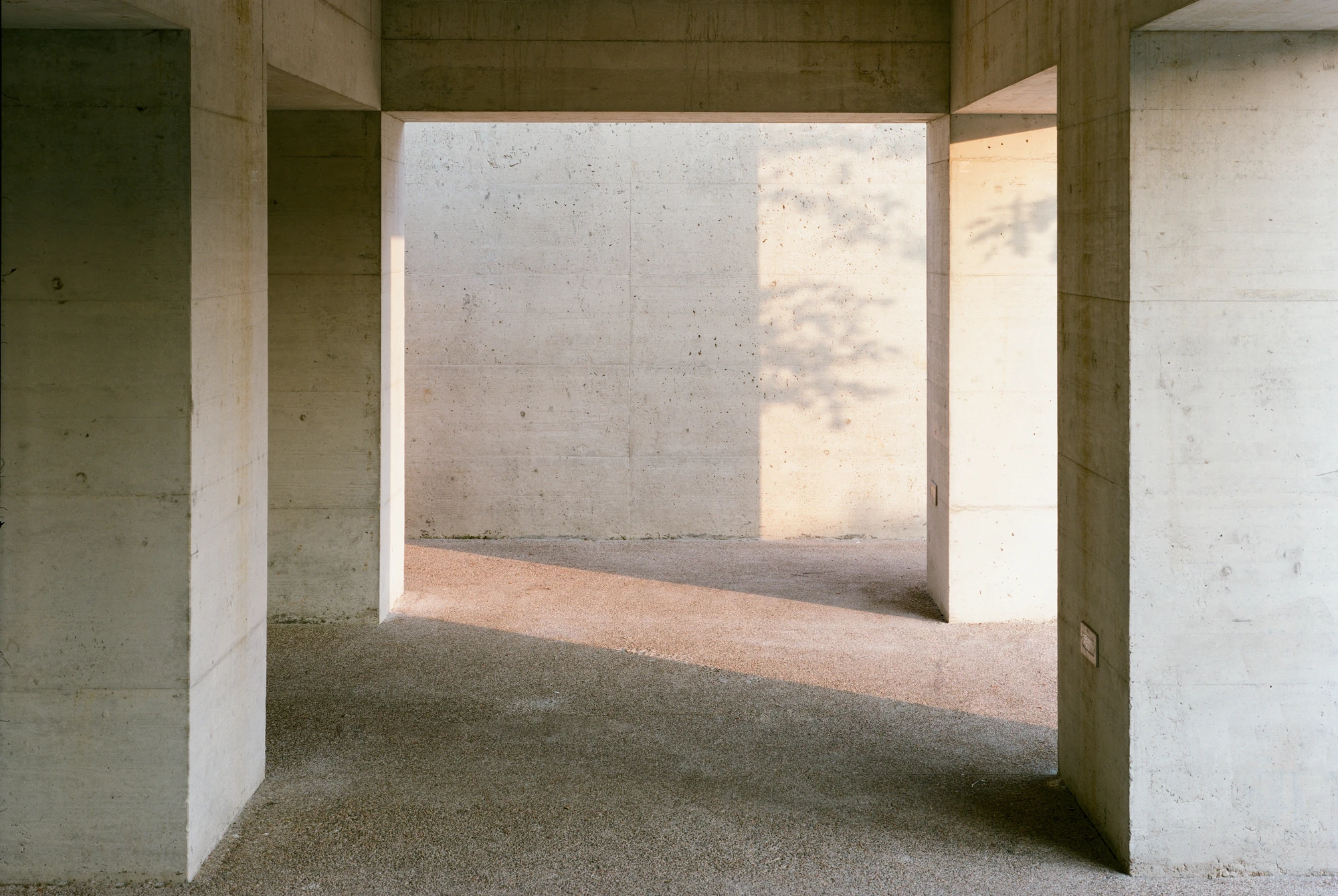 Biot Municipal Building Extension by Atelier EGR, photographed by Giaime Meloni — A passage cut through the concrete structure, sunlight and leaf shadow falling on the far wall.