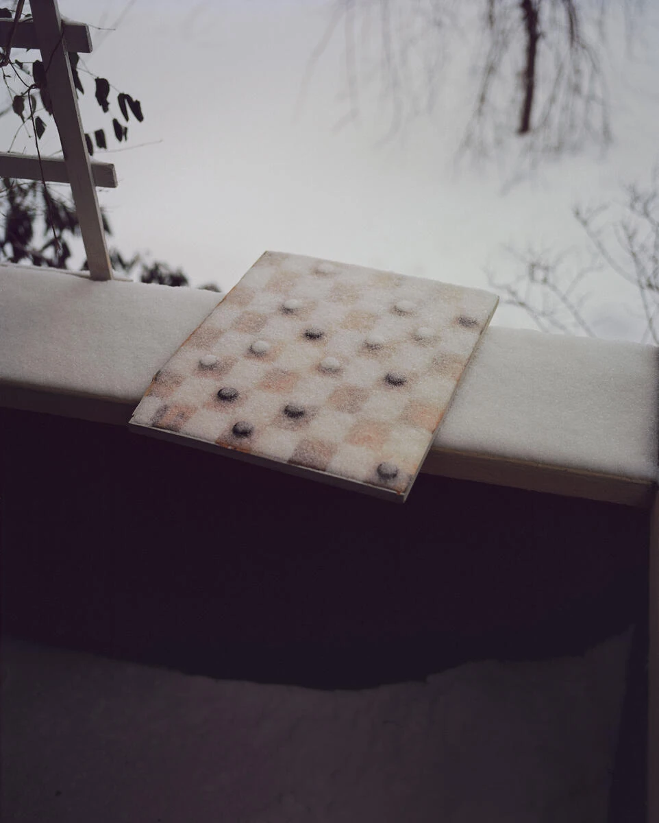 King, Queen, Knave by Gregory Halpern, photographed by Gregory Halpern — A checkerboard dusted with snow rests on a snow-covered ledge, its pieces set out and half buried.