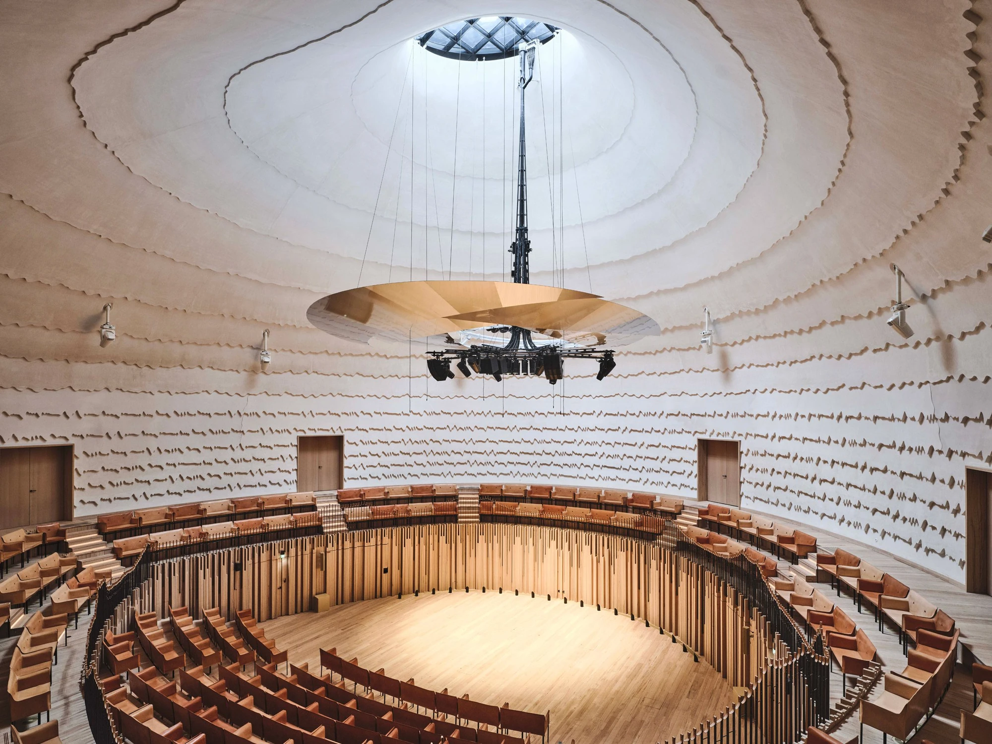 La Source Vive by PCA-Stream, photographed by PCA-Stream — The domed auditorium seen from the upper tier, with a glazed oculus at the crown and a gold aluminium canopy suspended above the circular timber stage.