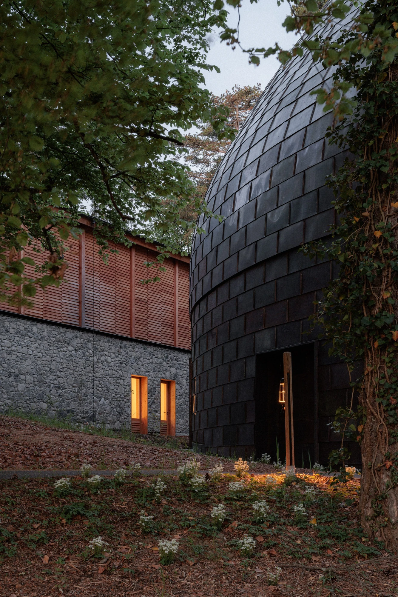 La Source Vive by PCA-Stream, photographed by PCA-Stream — The copper-clad drum meeting a rubble stone base, with the louvred red timber wall of the neighbouring hall to the left.