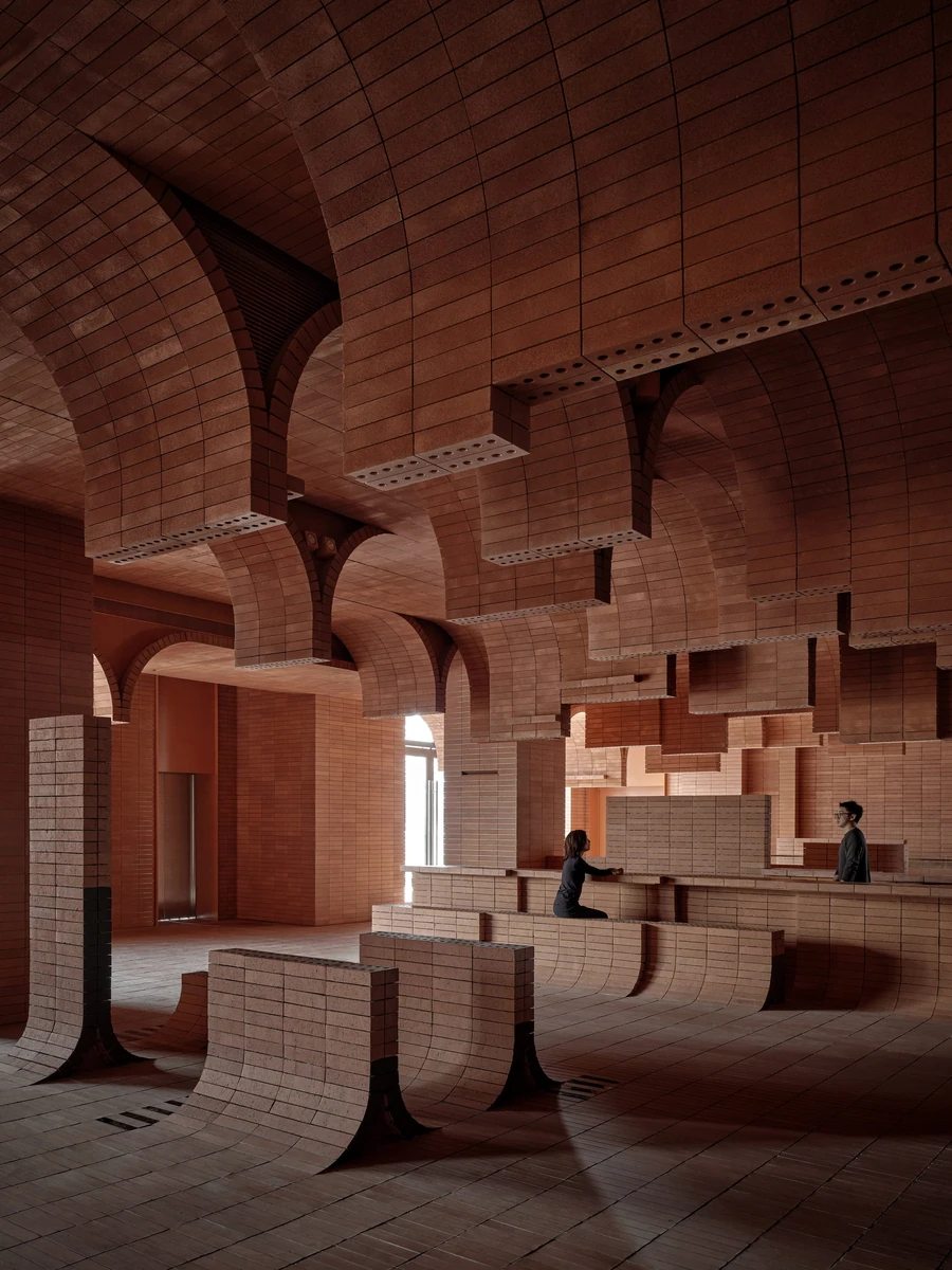 Haikou Gaoxingli Insun Cinema by One Plus Partnership, photographed by One Plus Partnership — Vertical view of the brick lobby, daylight entering beside a stainless steel lift door as vaults spring overhead and curved brick benches roll off the floor.