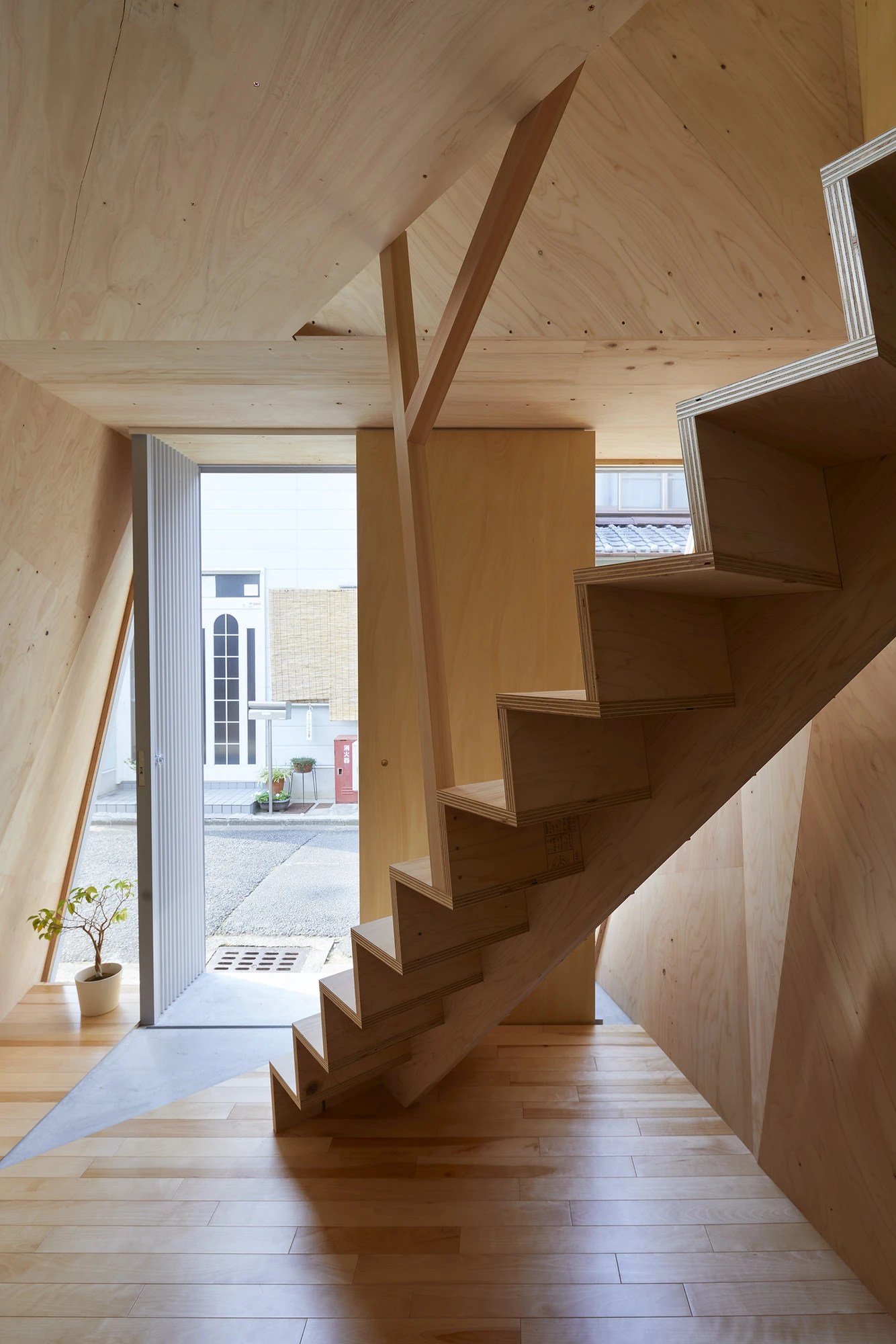 24mm Plywood House by Alphaville Architects, photographed by Alphaville Architects — Plywood stair with open zigzag treads rising past a wide horizontal window that frames the street, walls and floor lined in pale structural plywood with a birch strip…
