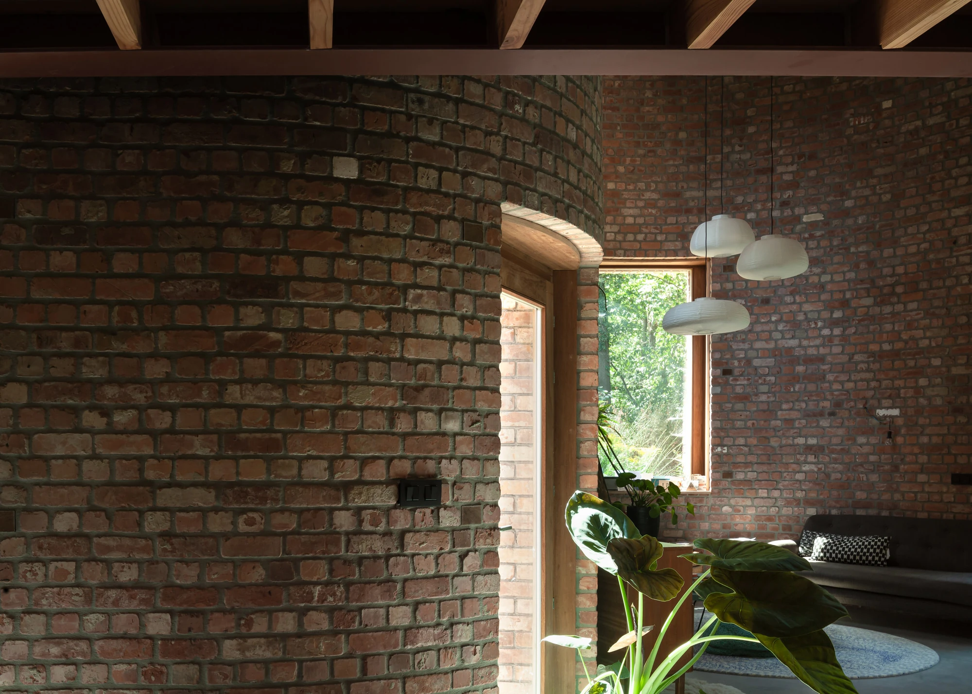 GjG House by BLAF Architecten, photographed by BLAF Architecten — A curved brick pier turning into a timber-framed doorway, paper pendants and the seating area visible beyond.