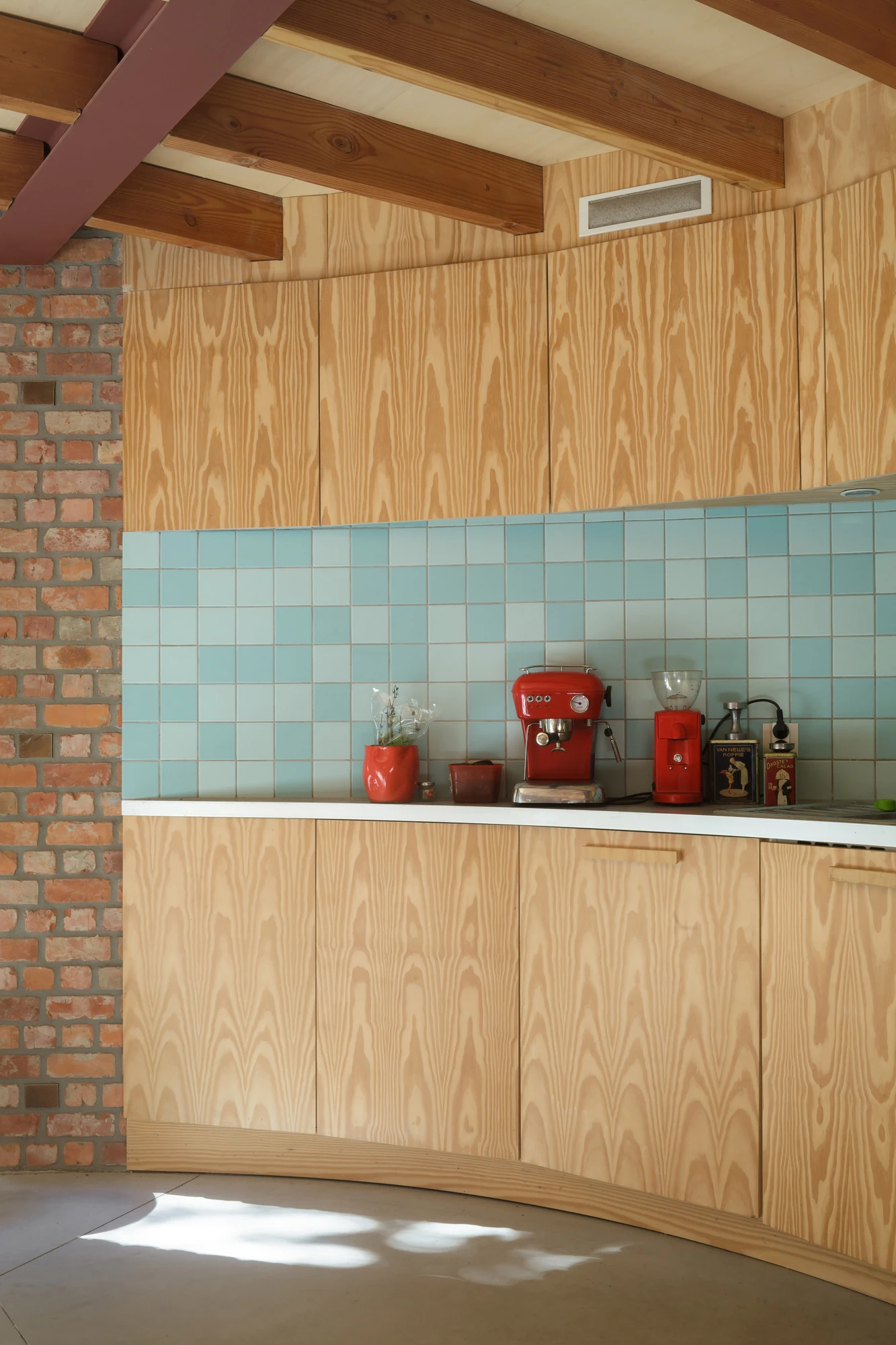 GjG House by BLAF Architecten, photographed by BLAF Architecten — Kitchen detail, pine plywood cabinetry with looping grain, a two-tone blue tiled splashback and a red espresso machine and grinder on the counter.