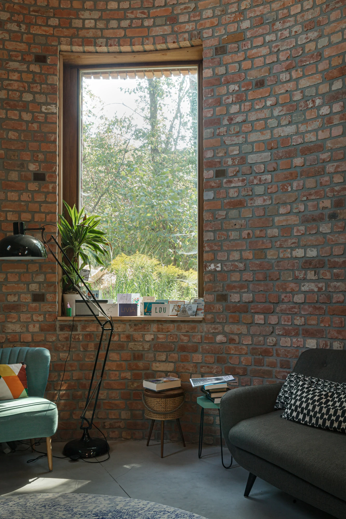 GjG House by BLAF Architecten, photographed by BLAF Architecten — Window sill lined with cards and a plant in the brick wall, an anglepoise floor lamp standing between a mint armchair and a grey sofa.