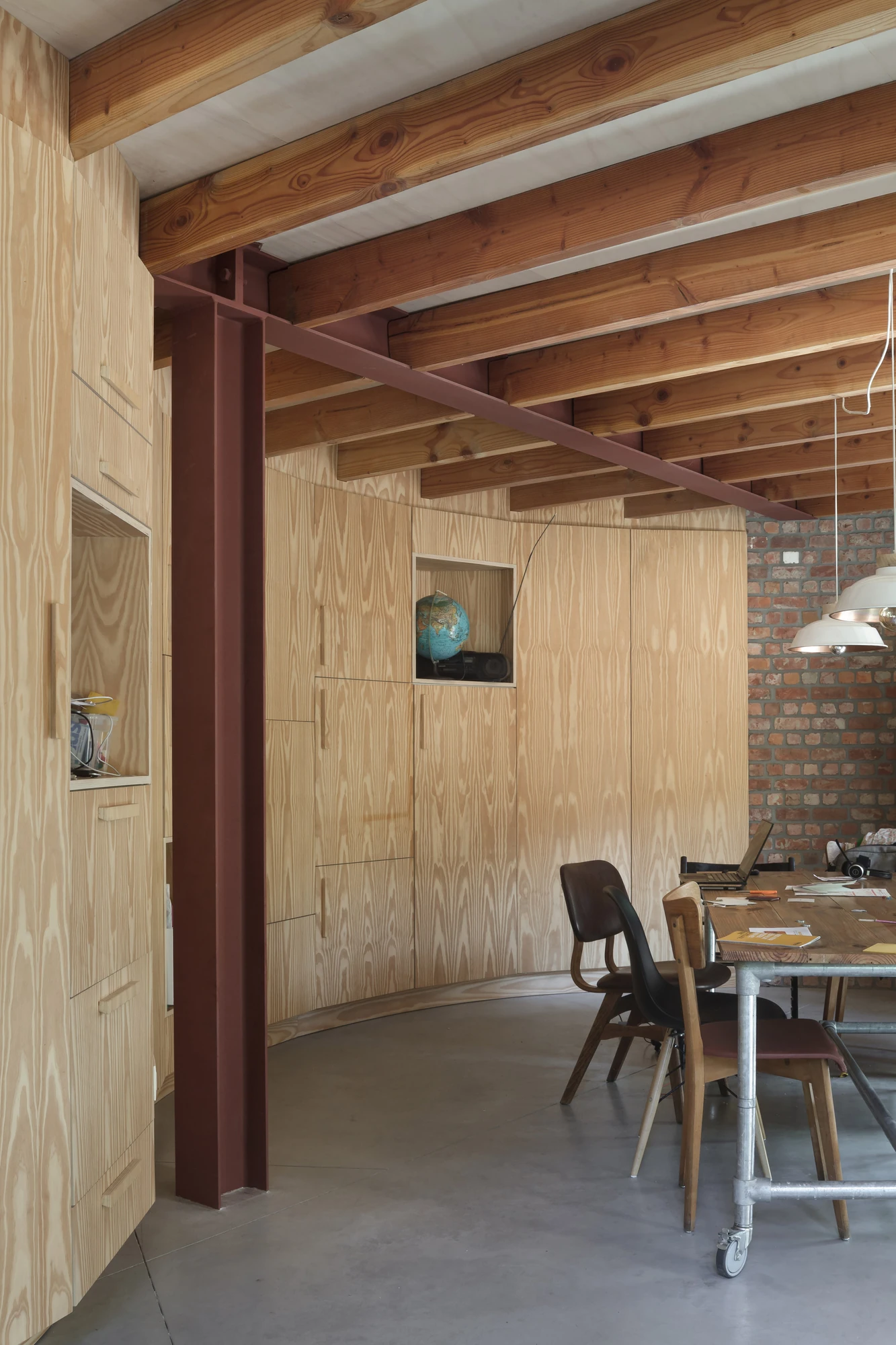 GjG House by BLAF Architecten, photographed by BLAF Architecten — Dining area with a curved plywood storage wall, a small niche holding a globe, an oxblood steel column and a wooden table with mismatched chairs.