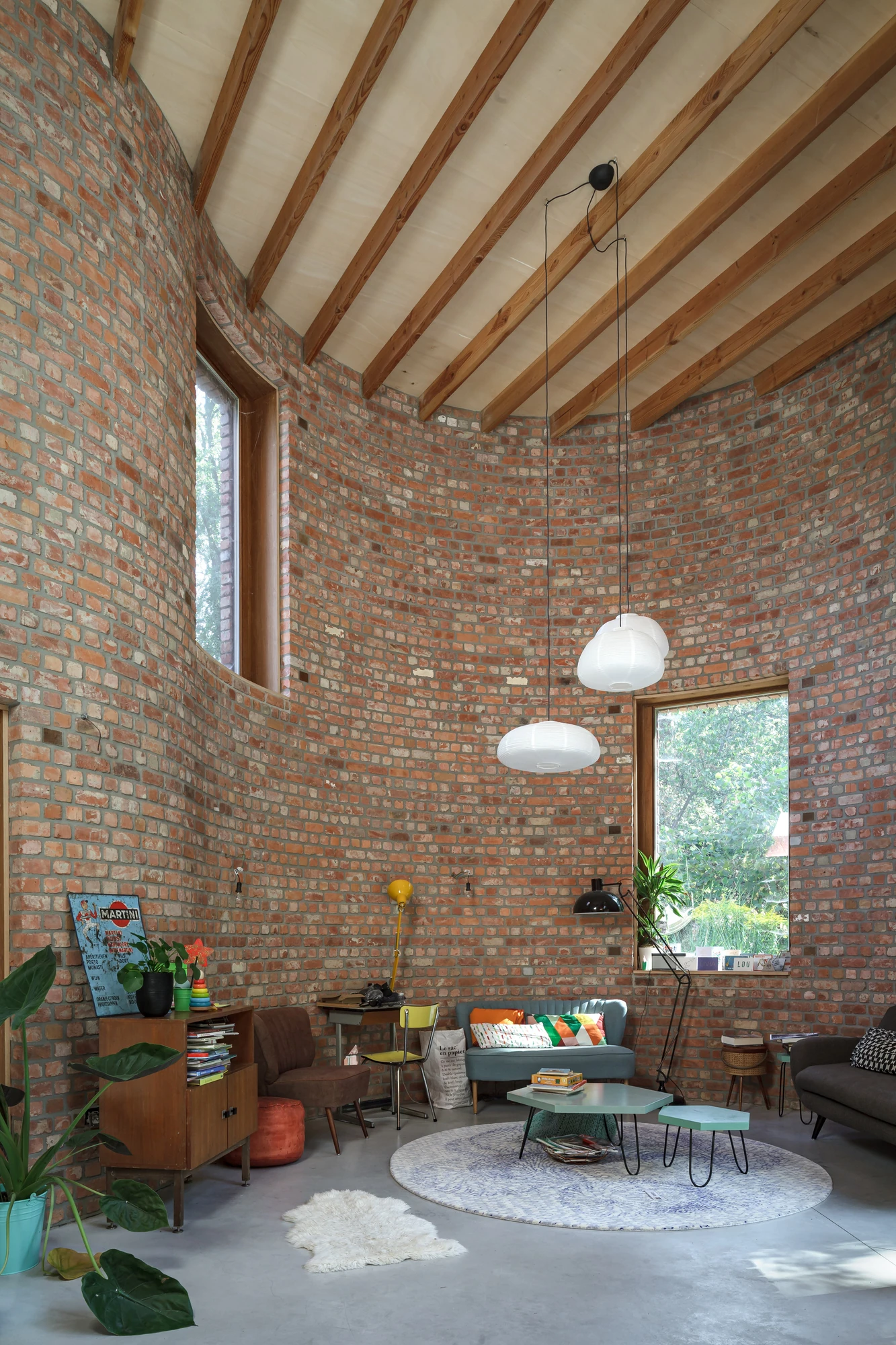 GjG House by BLAF Architecten, photographed by BLAF Architecten — Double-height living room, bare reclaimed brick curving up to pine rafters and a plywood ceiling, two paper pendants hanging above a low blue sofa.