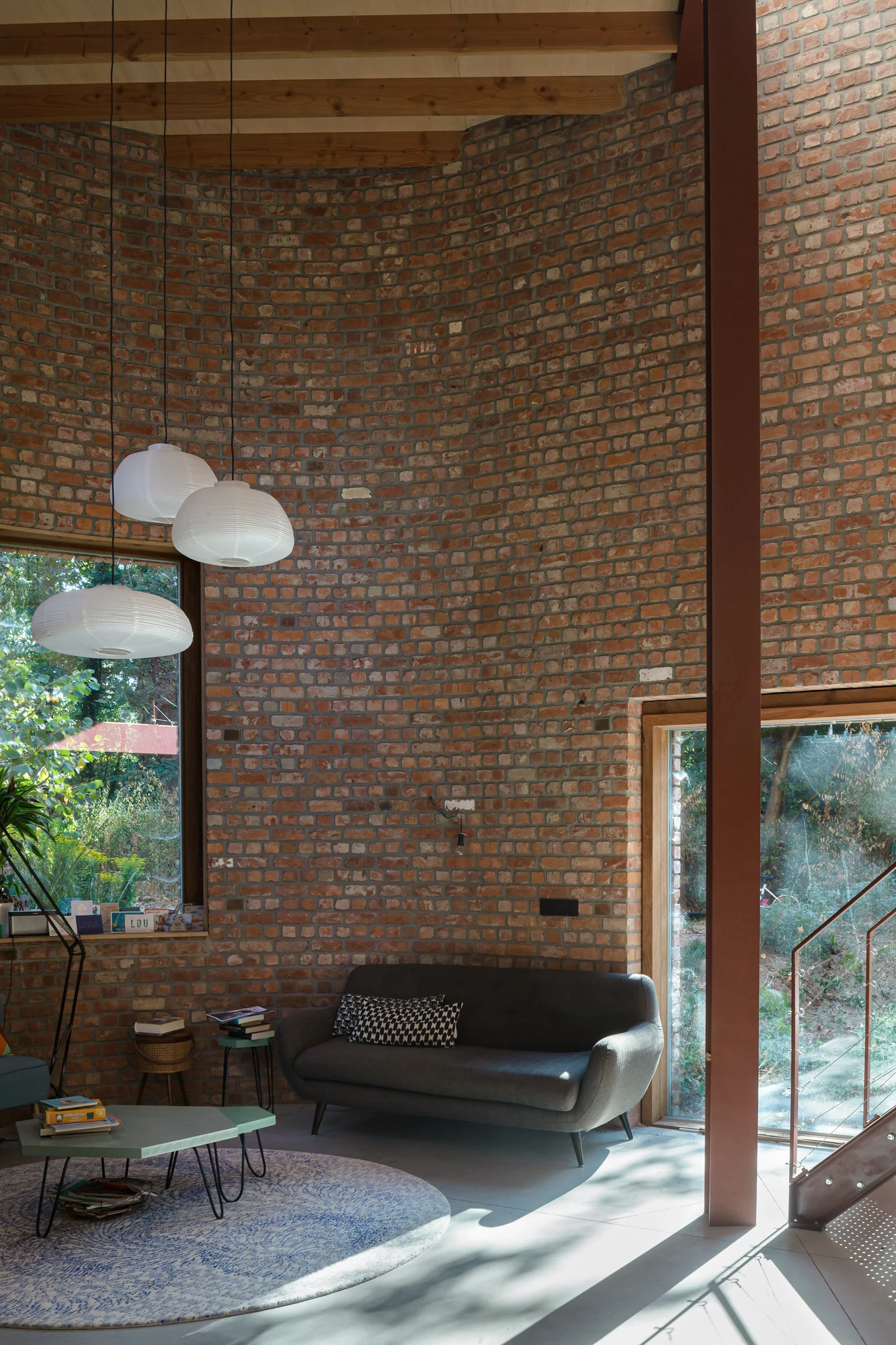 GjG House by BLAF Architecten, photographed by BLAF Architecten — Living area with a grey sofa against the curved brick wall, three paper pendants overhead and a glazed door opening to the garden stair.