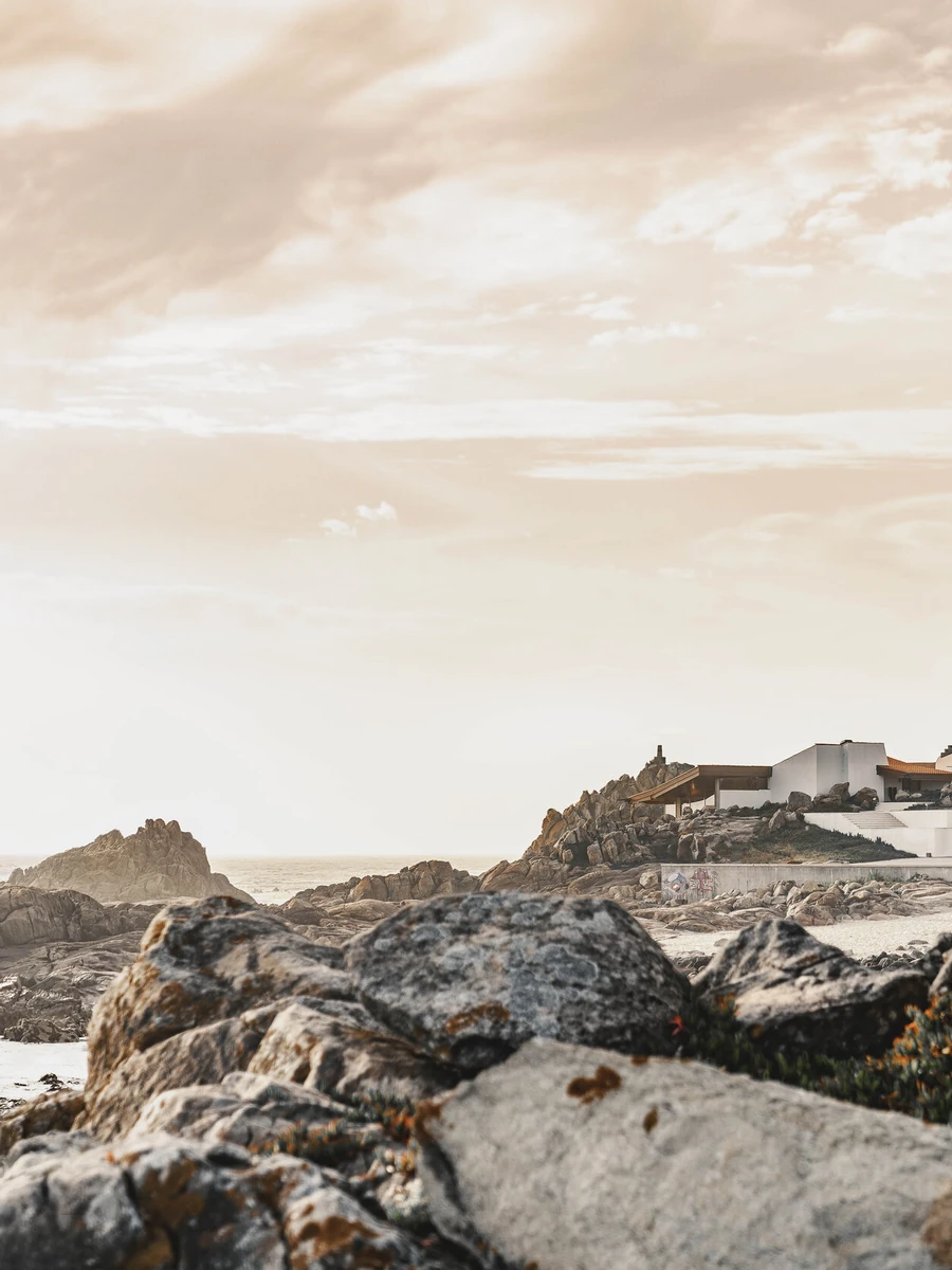 Casa de Chá da Boa Nova by Álvaro Siza, photographed by Nick Dearden — Wide view along the rocky Atlantic shore at low tide, the white volumes and tiled roof of the tea house set on a granite outcrop in the far distance.