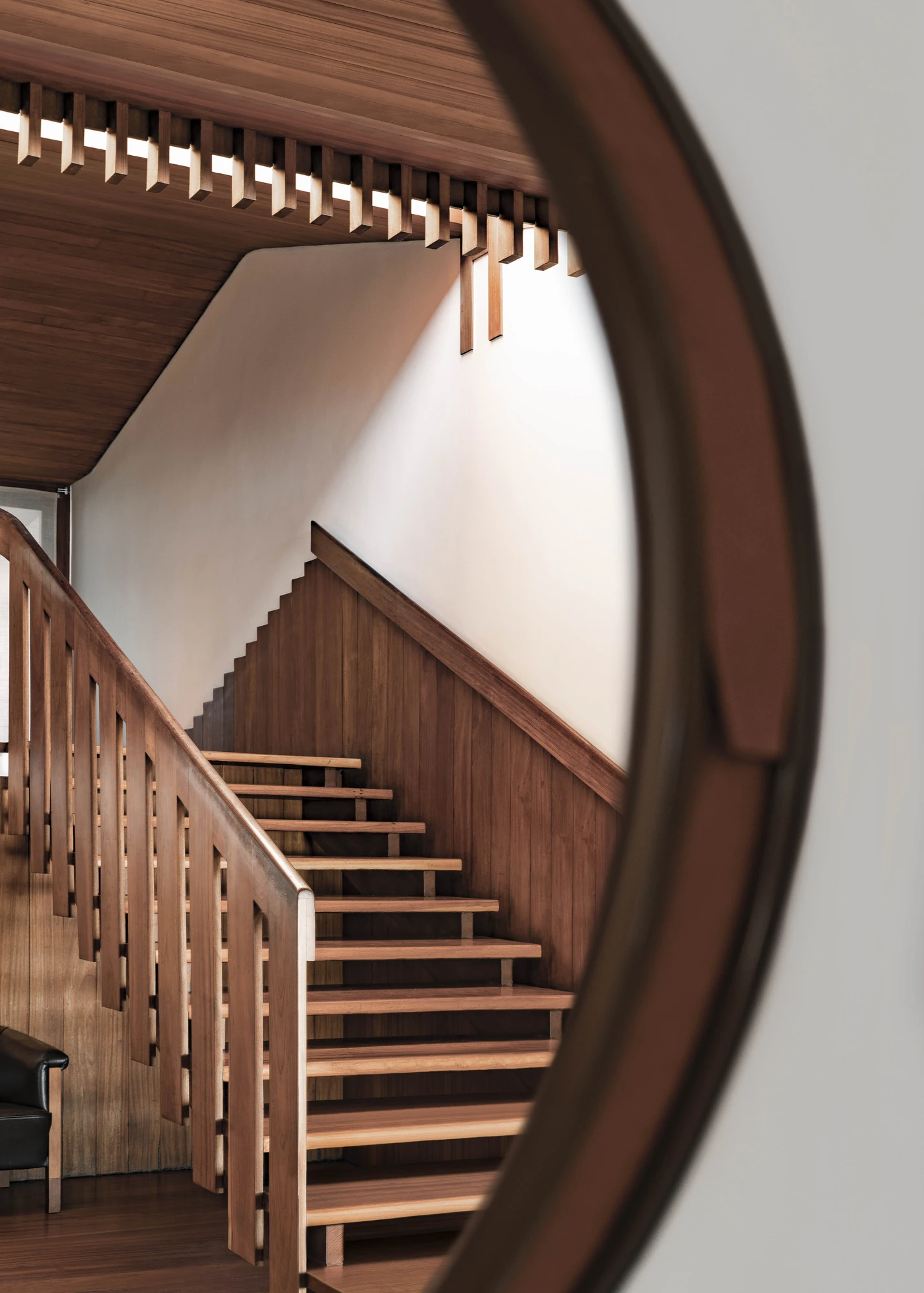 Casa de Chá da Boa Nova by Álvaro Siza, photographed by Nick Dearden — A round timber-framed mirror reflecting the main stair, with a slatted wood balustrade, panelled walls and a row of timber fins releasing light along the ceiling.
