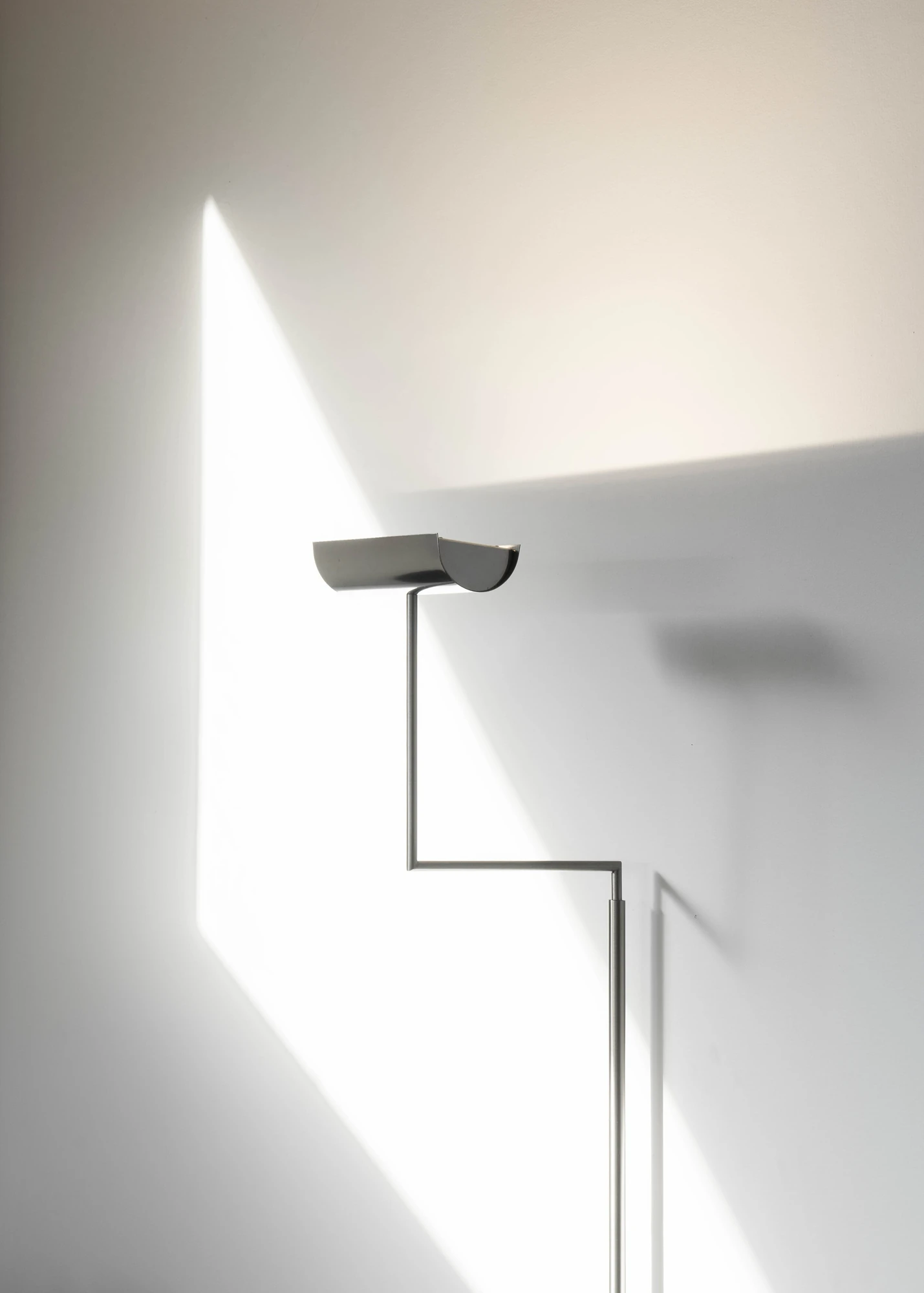 Casa de Chá da Boa Nova by Álvaro Siza, photographed by Nick Dearden — A slim uplighter with a half-cylinder shade against a bare plastered wall, a hard-edged shaft of daylight crossing the corner behind it.