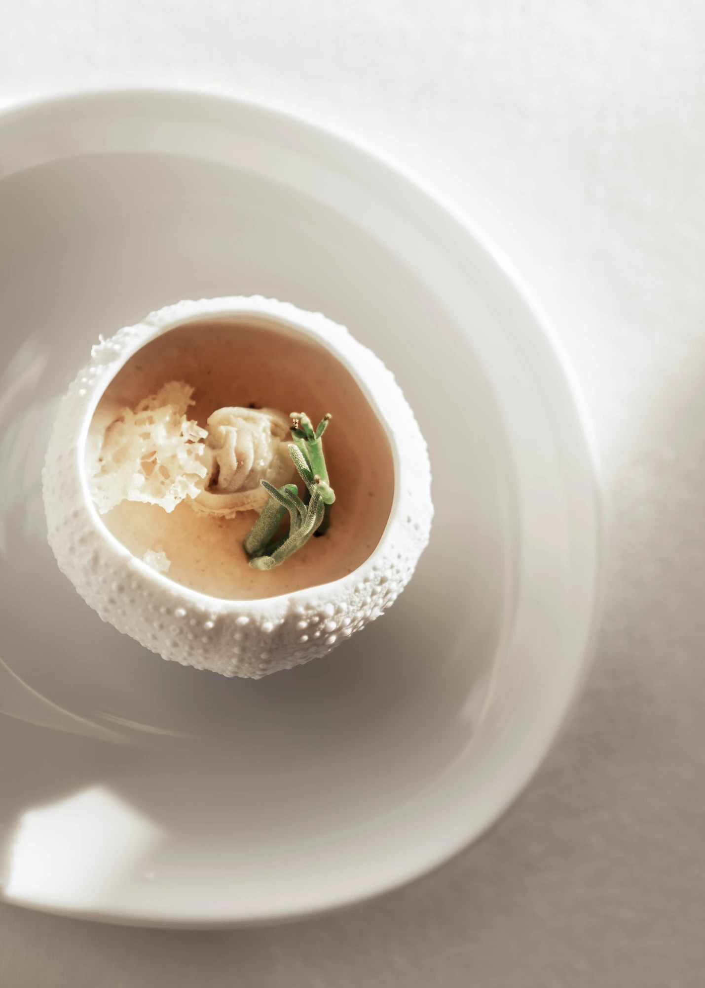Casa de Chá da Boa Nova by Álvaro Siza, photographed by Nick Dearden — Broth and shellfish served in a textured porcelain sea urchin, dressed with sea greens and salt flakes and set in a wide white bowl.
