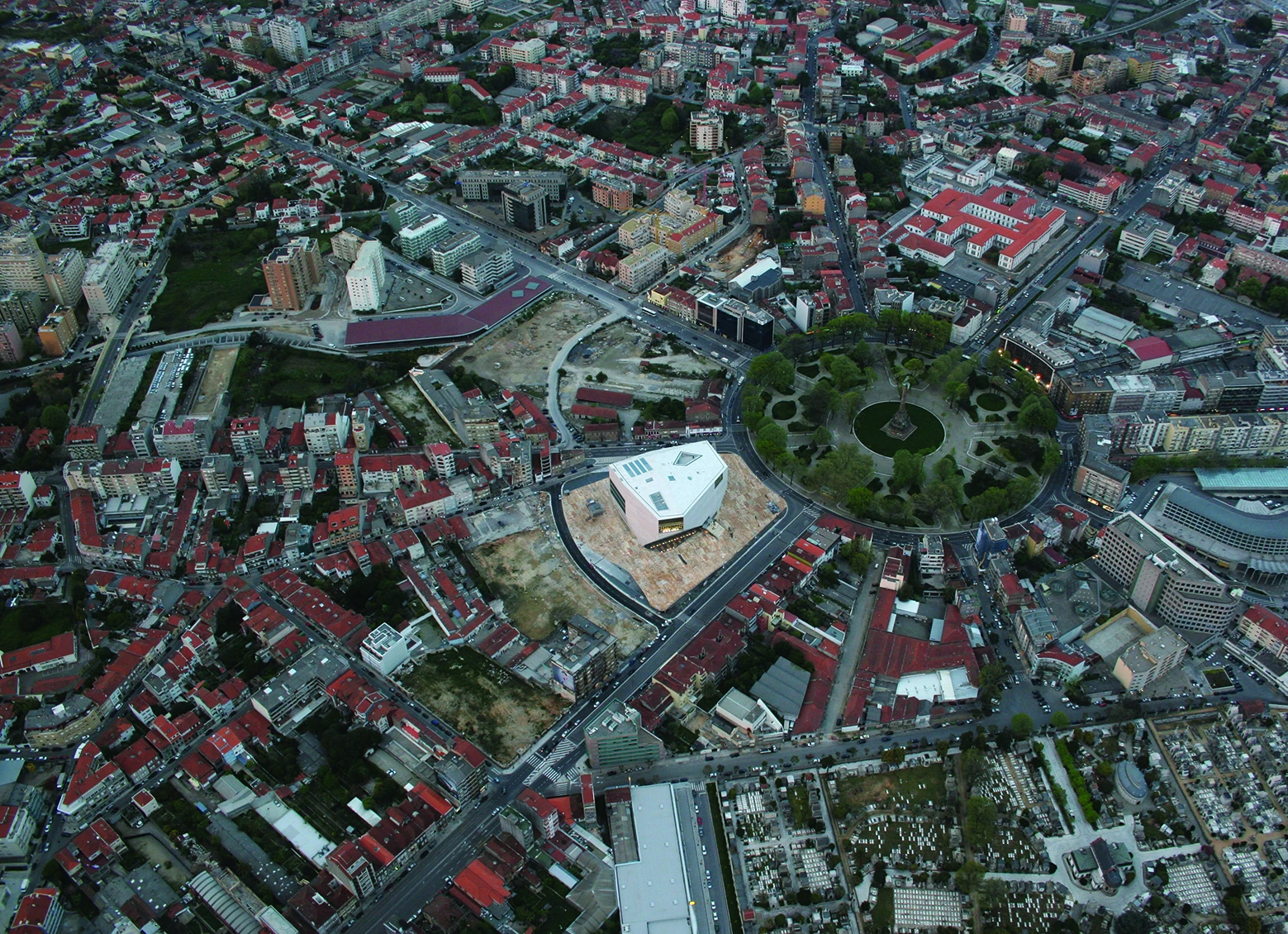 Casa da Música by OMA, photographed by Philippe Ruault — Wide aerial of the Boavista roundabout, the white block standing alone on its cleared plateau beside the circular park and the red roofs of Porto.