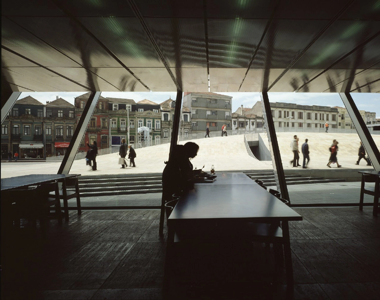 Casa da Música by OMA, photographed by Philippe Ruault — The ground floor restaurant looking out through raking glazing at the travertine plaza and the painted nineteenth century facades across the street.