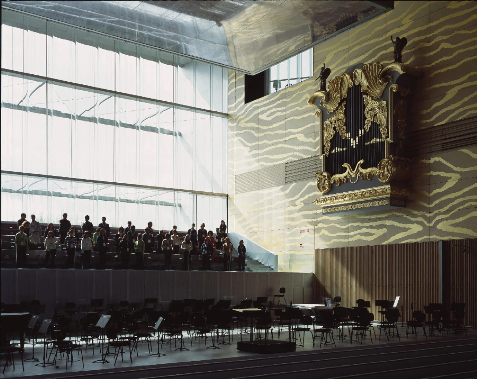 Casa da Música by OMA, photographed by Philippe Ruault — Daylight through the corrugated glass end wall of the main hall, a gilded organ case mounted on gold embossed plywood and visitors standing at the rear balcony.