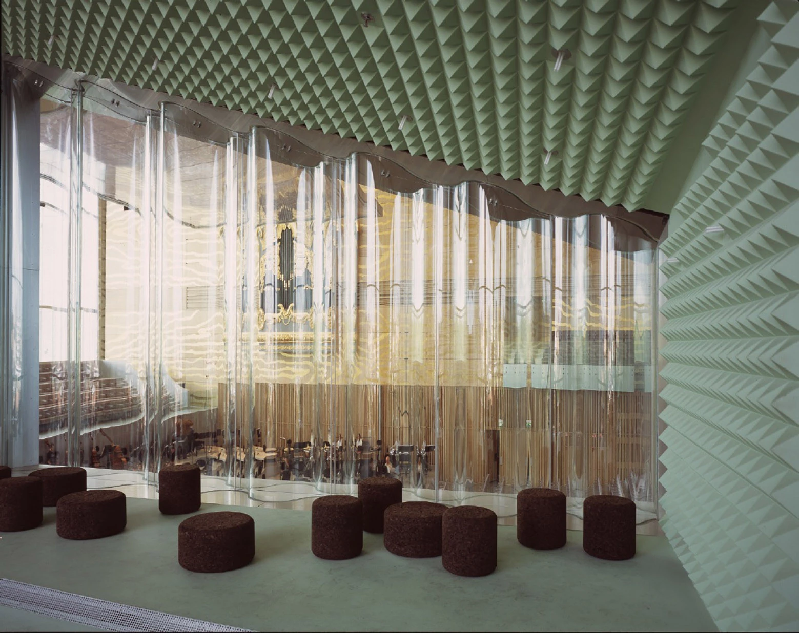 Casa da Música by OMA, photographed by Philippe Ruault — A rehearsal room lined in mint green acoustic pyramids, divided from the main hall by a curtain of clear corrugated glass, cork stools on the floor.