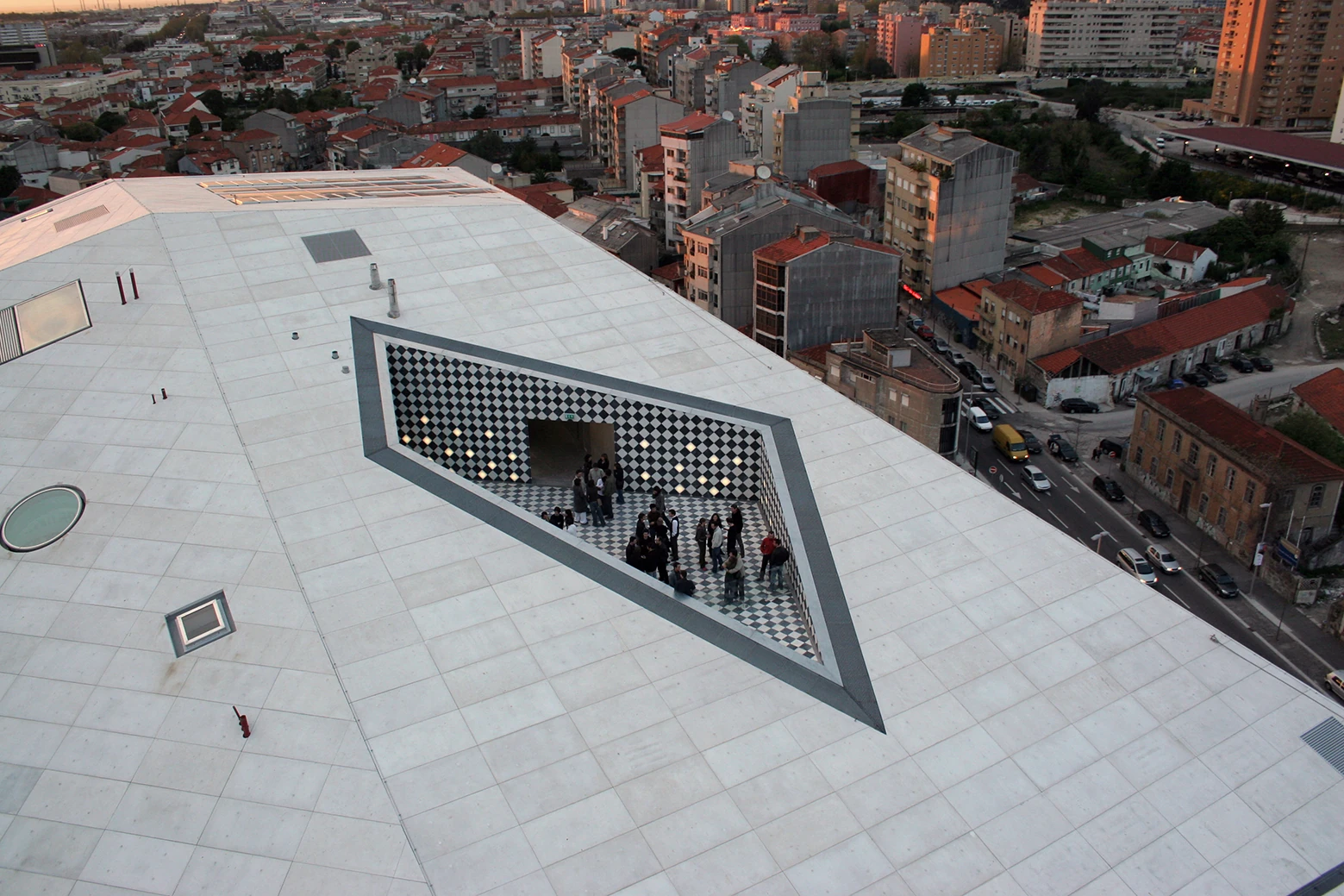 Casa da Música by OMA, photographed by Philippe Ruault — Looking down on the white roof plane, a trapezoid terrace cut into it and tiled in black and white diamonds, a group of visitors gathered inside.