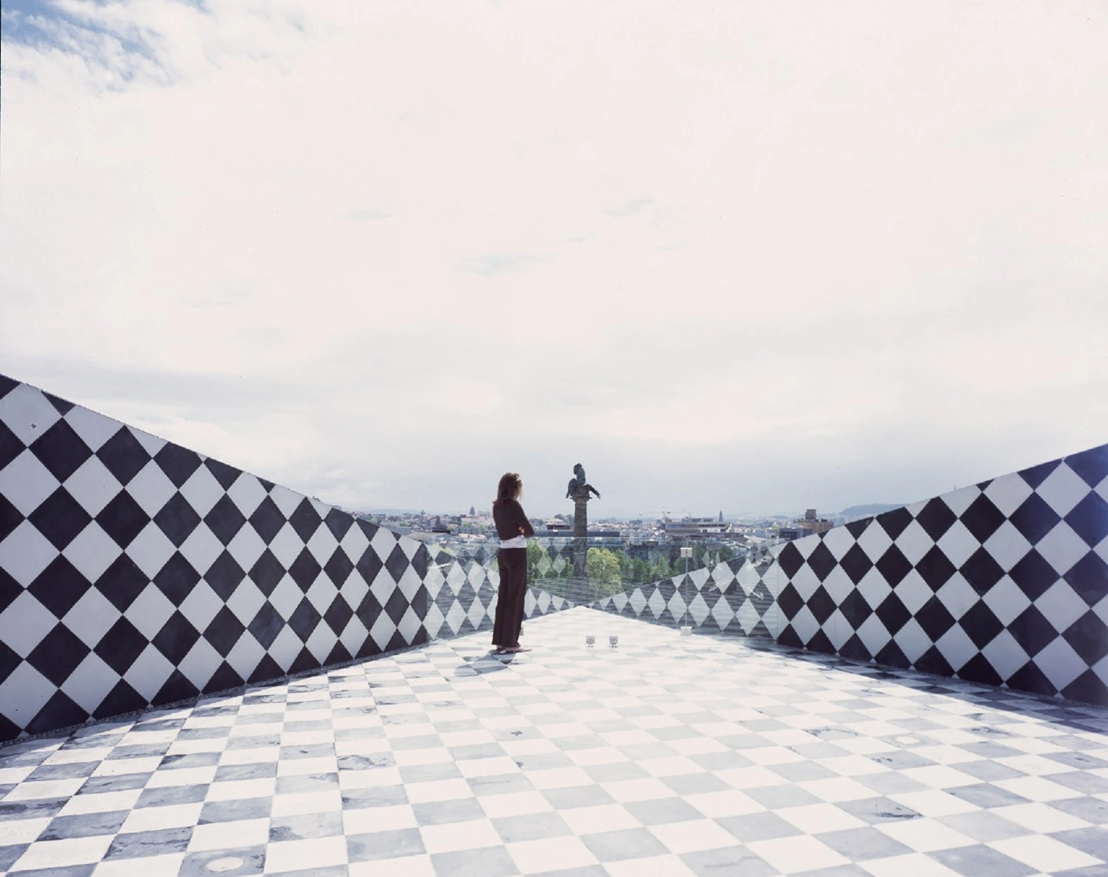 Casa da Música by OMA, photographed by Philippe Ruault — The roof terrace at eye level, black and white diamond tiled walls converging on a marble chequerboard floor, one figure at the parapet facing the bronze lion column.