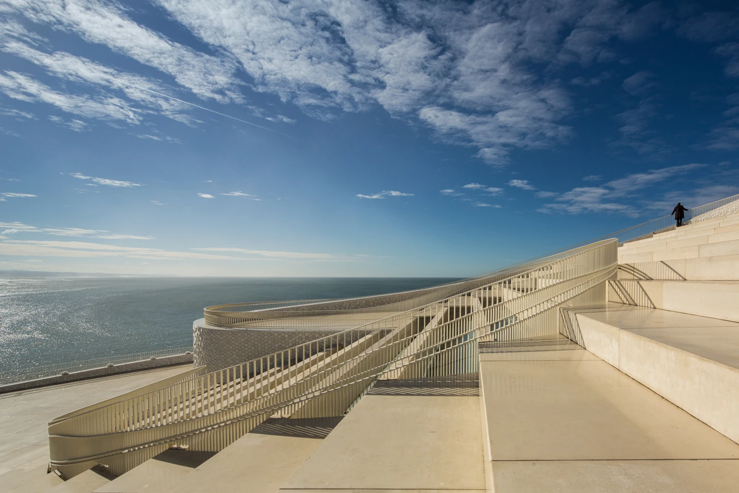 Leixões Cruise Terminal by Luís Pedro Silva Arquitecto, photographed by Fernando Guerra FG+SG — The public roof steps down toward the Atlantic, its ramp and railings curving back on themselves, a lone figure at the top of the steps.