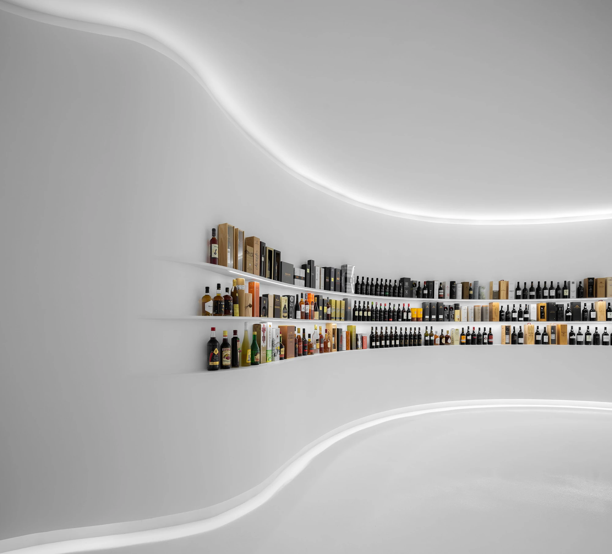 Portugal Vineyards Concept Store by Porto Architects, photographed by Ivo Tavares Studio — Shelves emerge from the blank white wall and taper away to nothing at their ends, carrying boxed wines and spirits between two lines of concealed light.