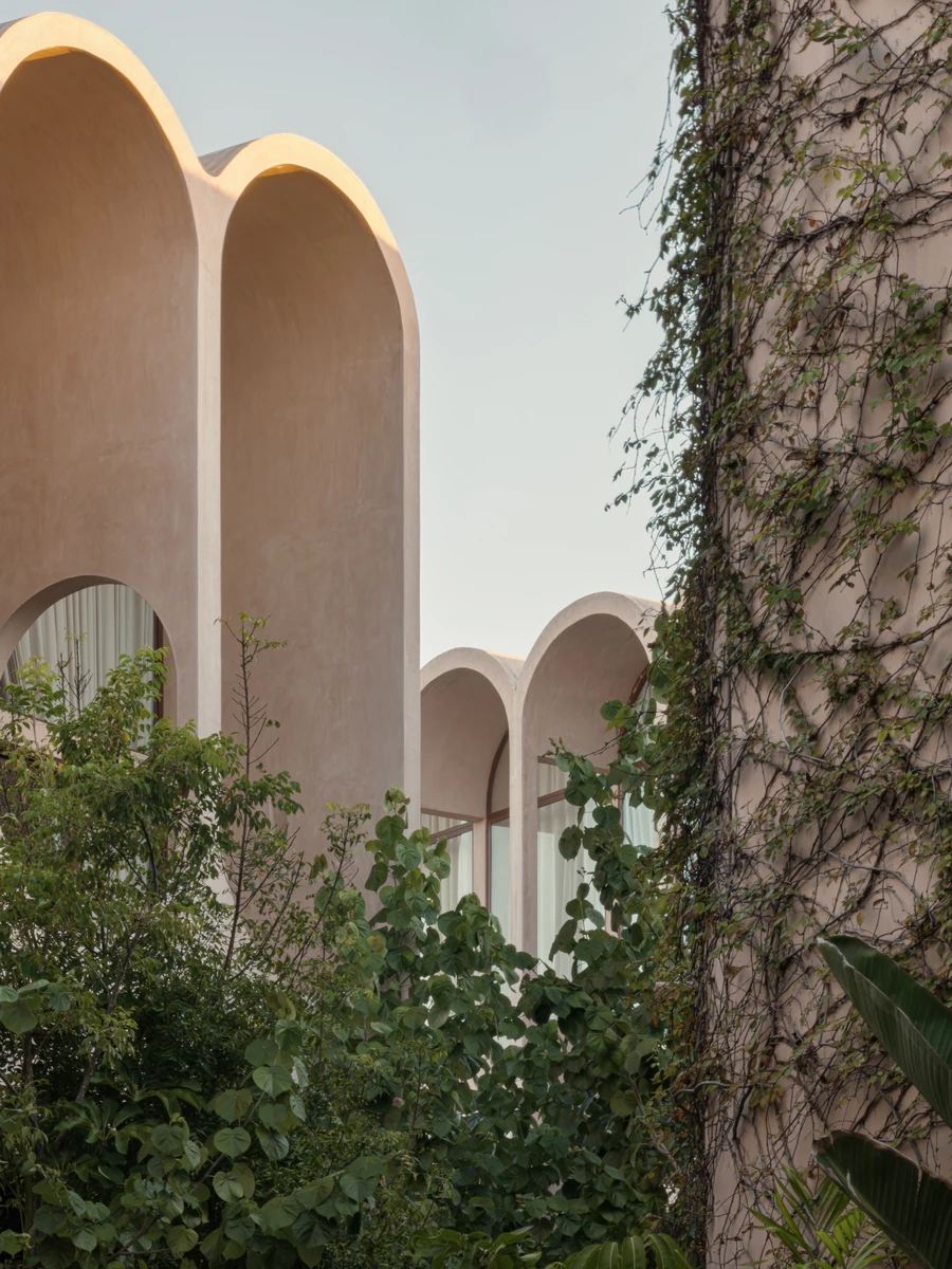 Babel by V Taller, photographed by Funciono — Tall arch profiles in pale chukum plaster catch late sun against the sky, with a curved wall dense in climbing vines to one side.