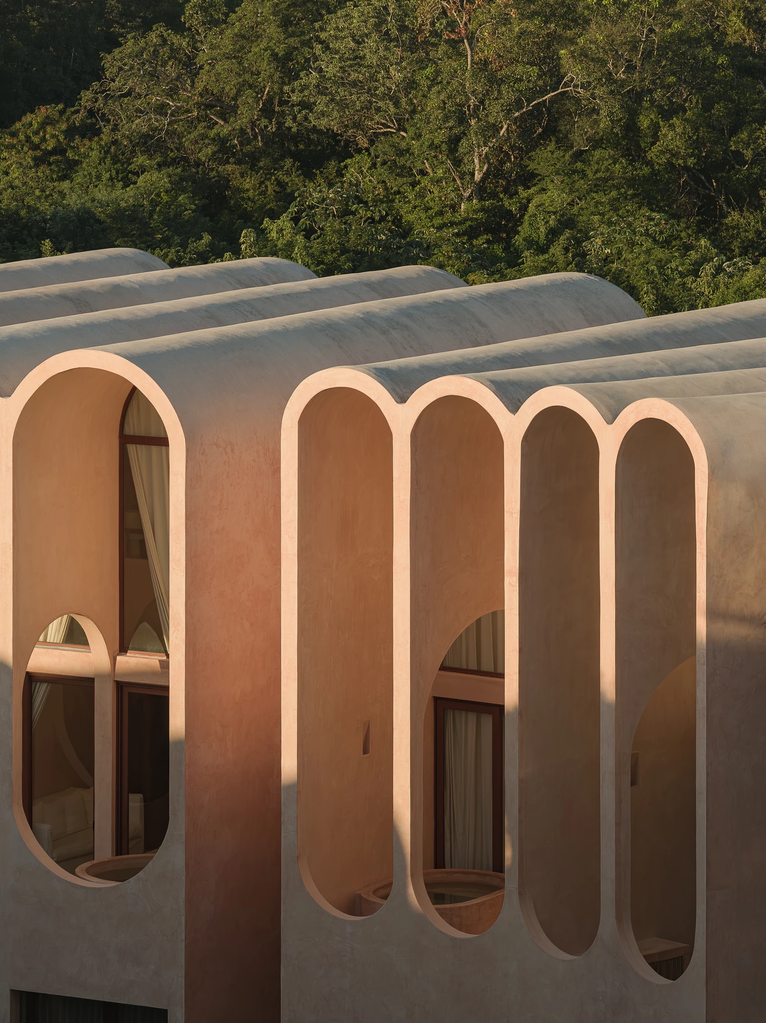 Babel by V Taller, photographed by Funciono — Raking evening light across the facade, slender arch profiles set against grey-toned barrel vaults, oval openings revealing curtained rooms behind.