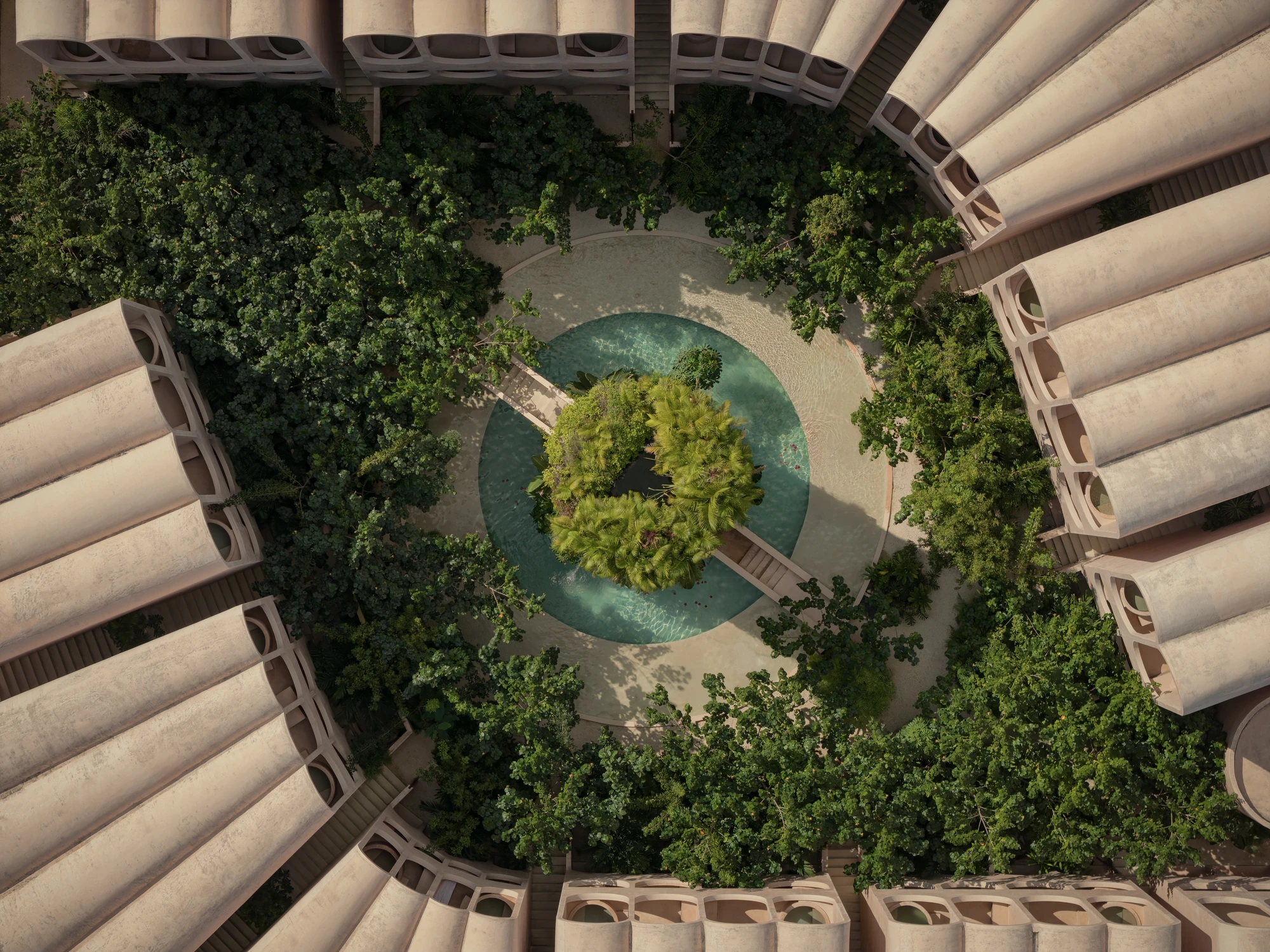 Babel by V Taller, photographed by Funciono — Seen from directly above, the two curved wings of vaulted roofs close around a planted courtyard and a circular pool with a palm island at its centre.