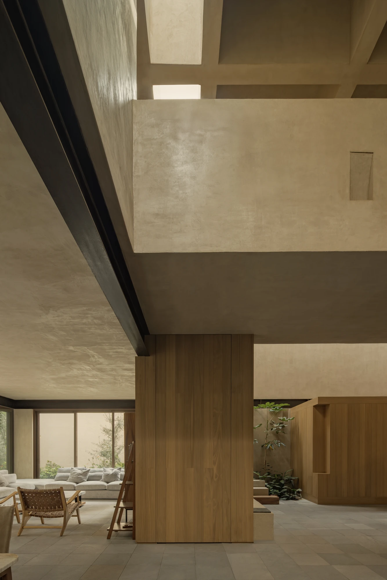 Casa Azaleas by V Taller, photographed by Funciono — A black steel beam crosses the living area beside an oak core, linen sofas and woven leather sling chairs facing a young tree in the court.