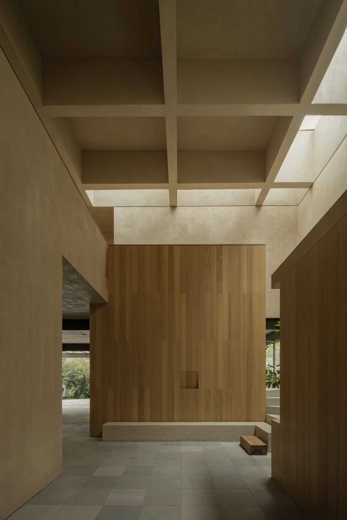 Casa Azaleas by V Taller, photographed by Funciono — An oak-clad volume set beneath a ribbed roof grid, skylights washing the beams, grey stone floor tiles running to a low aggregate concrete step.