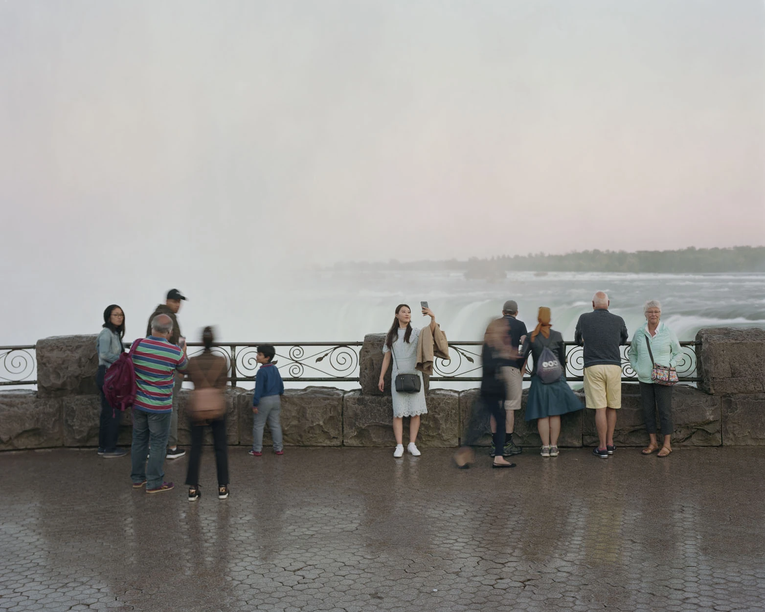 A Pound of Pictures by Alec Soth, photographed by Alec Soth — Tourists along a stone railing above Niagara Falls, one woman turning to photograph herself in the mist, from A Pound of Pictures by Alec Soth.