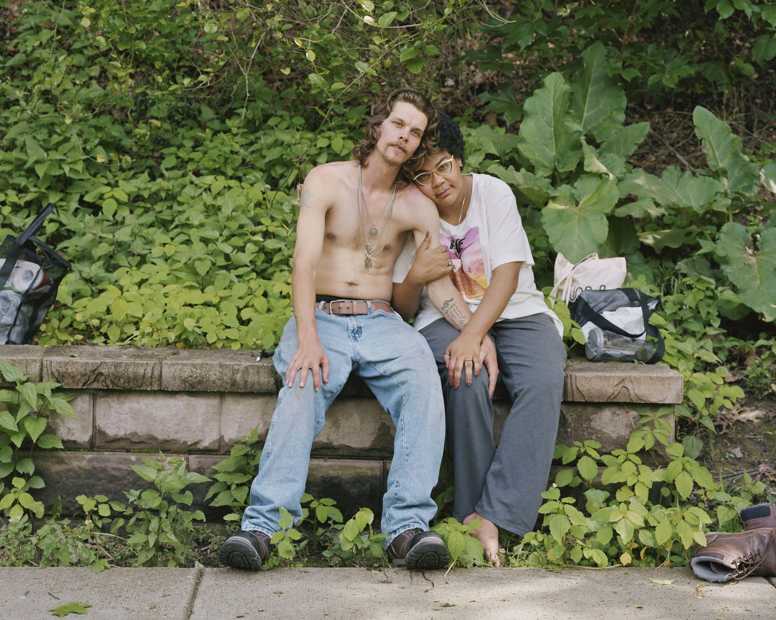A Pound of Pictures by Alec Soth, photographed by Alec Soth — A couple sit on a low stone wall in dense summer greenery, her head resting against his bare shoulder, from A Pound of Pictures by Alec Soth.