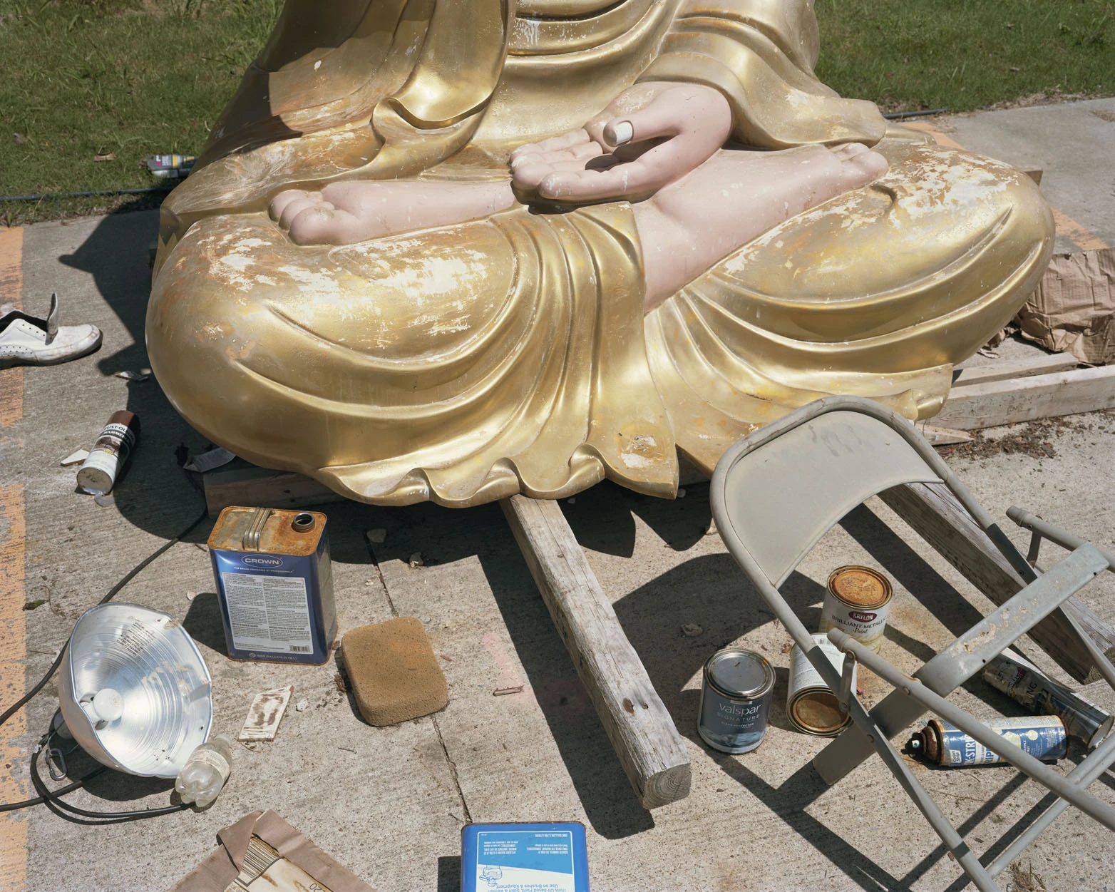A Pound of Pictures by Alec Soth, photographed by Alec Soth — A gold Buddha lies on its side on a concrete apron ringed by paint tins, spray cans and a folding chair, from A Pound of Pictures by Alec Soth.