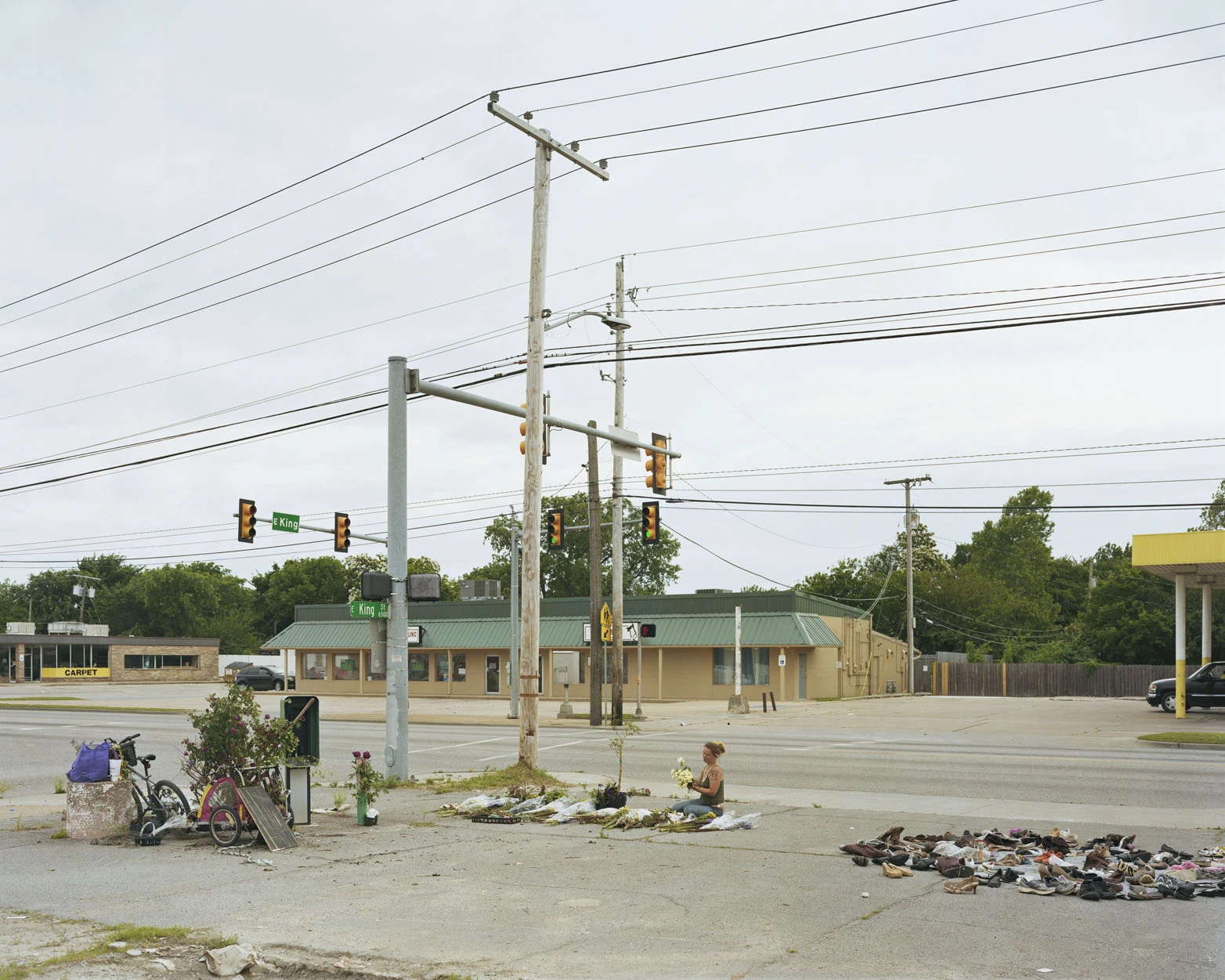A Pound of Pictures by Alec Soth, photographed by Alec Soth — A woman kneels among cut flowers at a roadside memorial while shoes lie scattered across the pavement nearby, from A Pound of Pictures by Alec Soth.