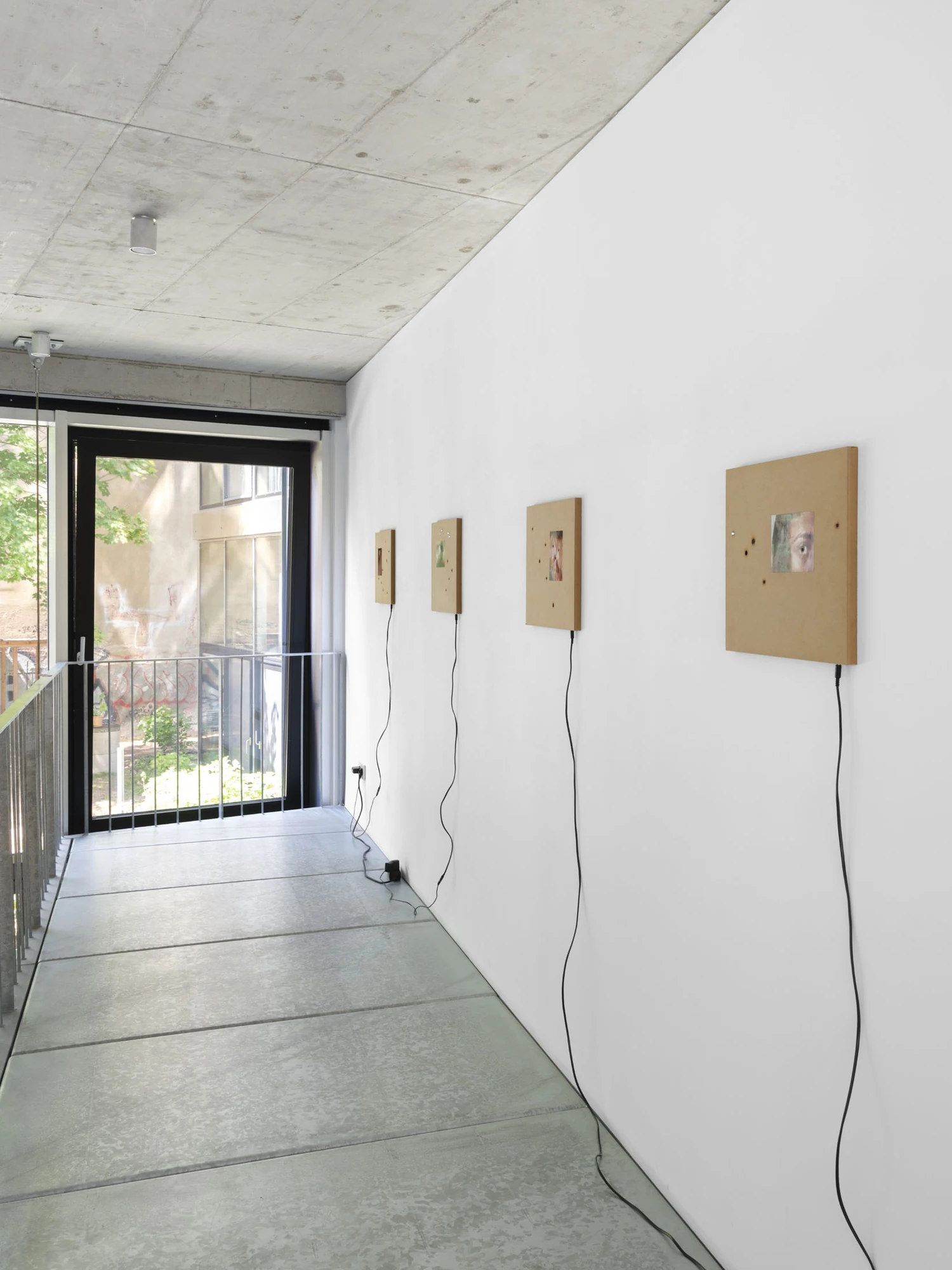 Apophenia by Galerie Molitor, photographed by Marjorie Brunet-Plaza — Four MDF panels with recessed screens line a white mezzanine wall, black cables trailing down to a socket by the glazing.