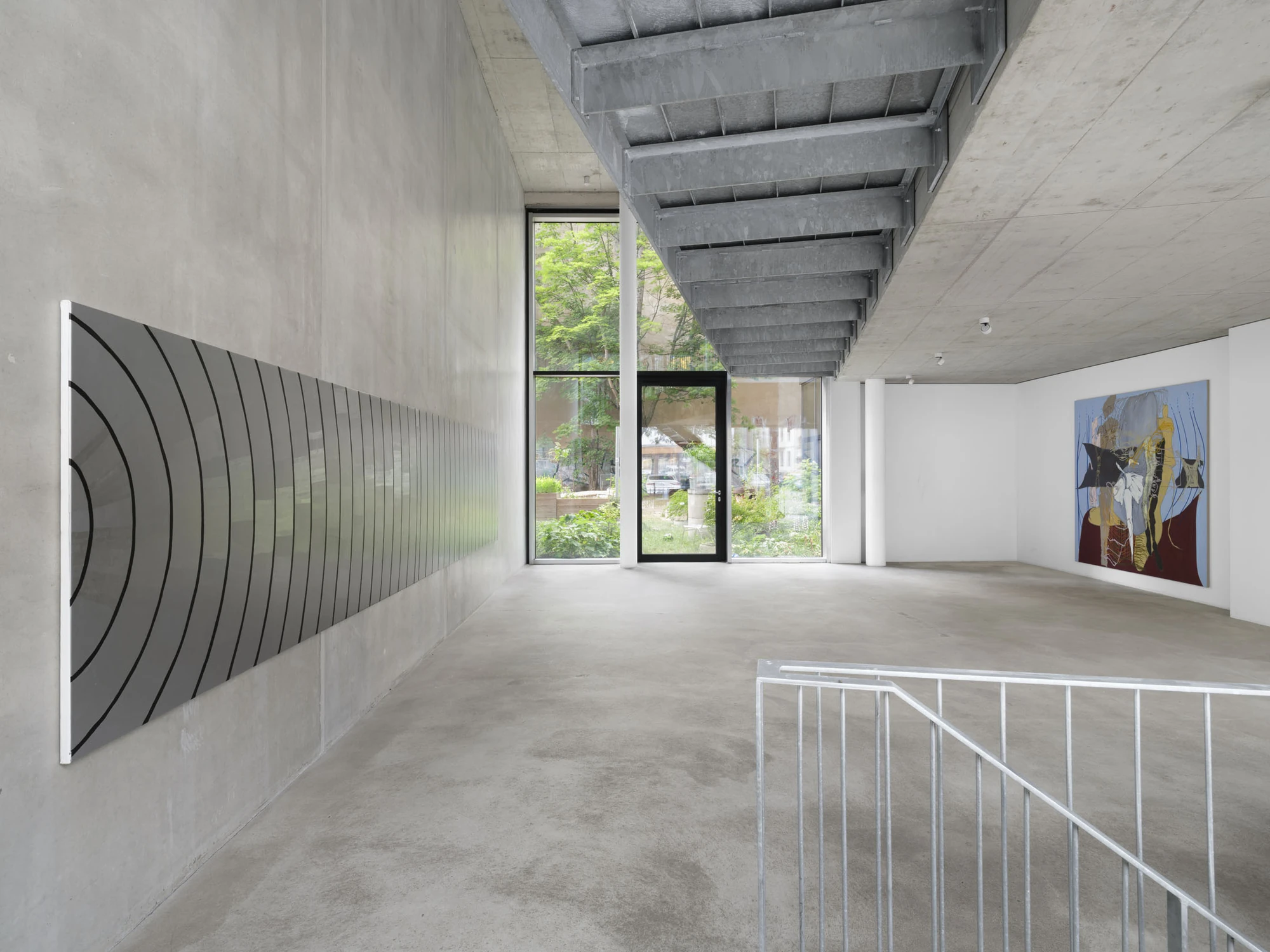 Apophenia by Galerie Molitor, photographed by Marjorie Brunet-Plaza — A grey panel scored with concentric black arcs runs along a concrete wall toward floor-to-ceiling glazing onto a green courtyard.