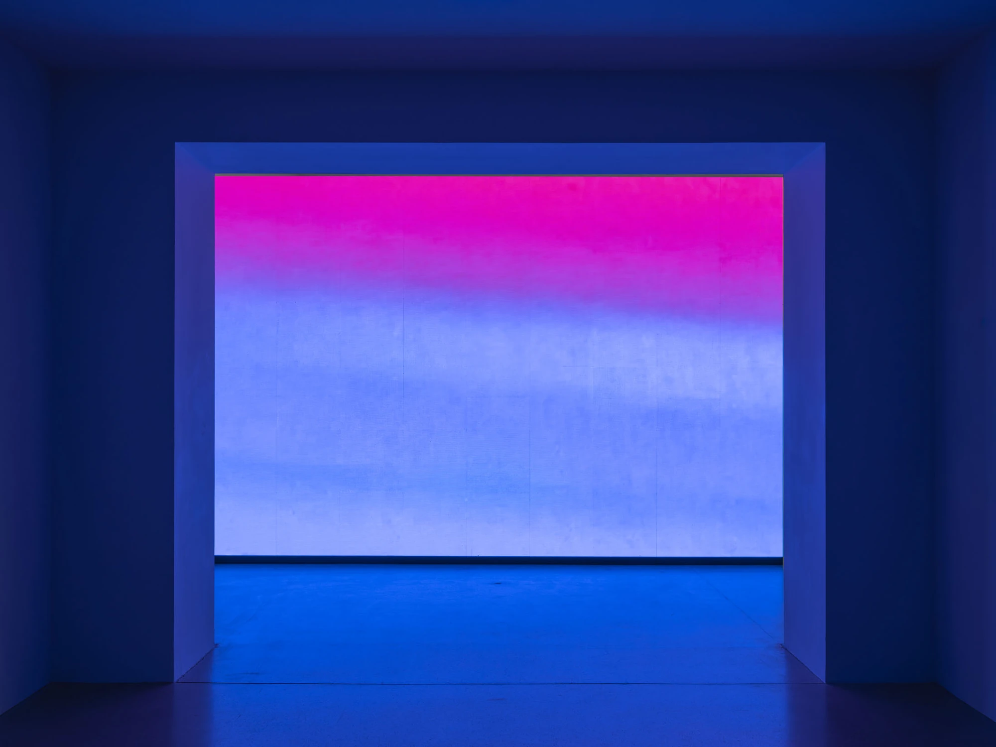 Dolls' Theater by Mimosa Echard, photographed by Julien Gremaud, Annik Wetter — Deep blue light floods a gallery antechamber; through a wide opening a wall-sized screen glows in a pink-to-blue gradient.