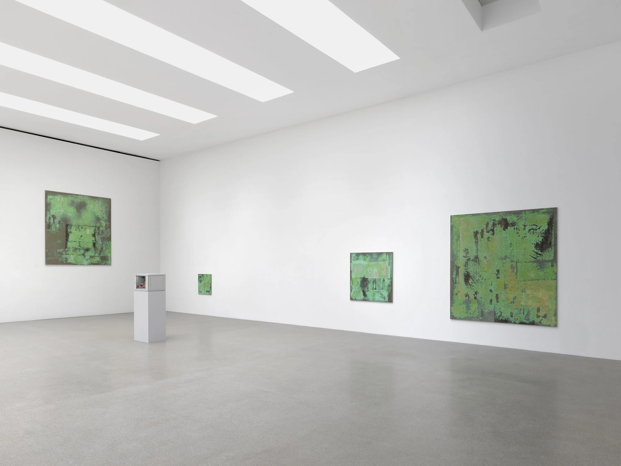 Dolls' Theater by Mimosa Echard, photographed by Julien Gremaud, Annik Wetter — Four oxidised green tableaux at varying scale hang across two white walls under strips of skylight, a grey vitrine on a plinth at left.