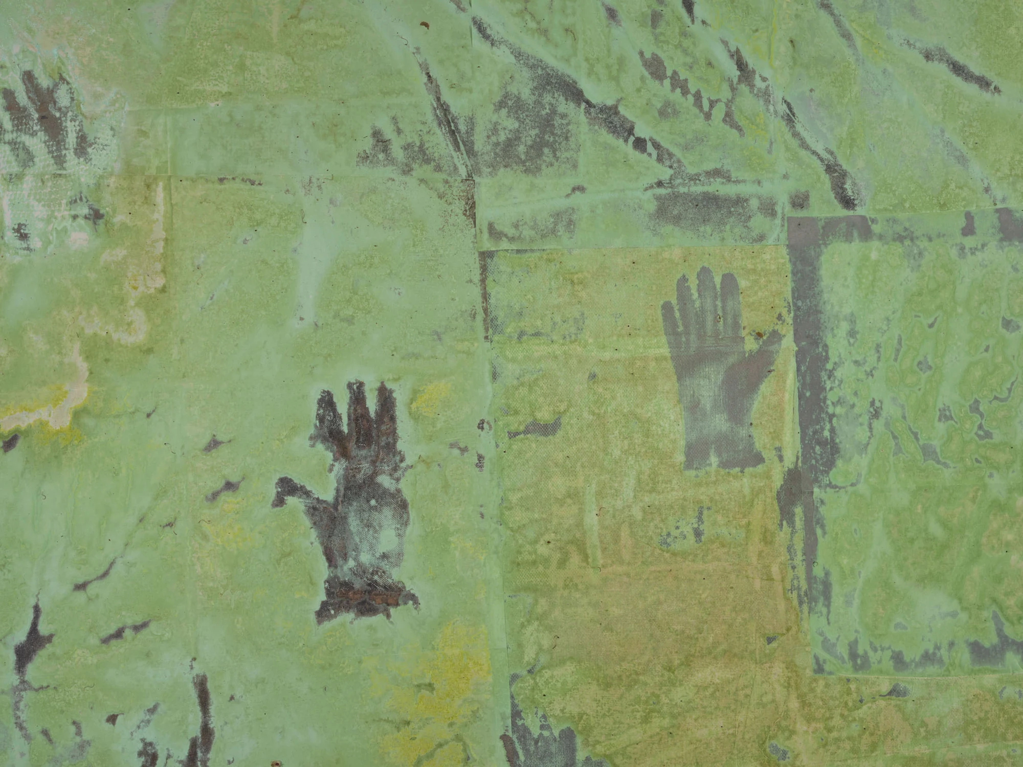 Dolls' Theater by Mimosa Echard, photographed by Julien Gremaud, Annik Wetter — Close view of patched shielding fabric oxidised to lime and olive, a grey glove print pressed into the surface beside a darker handprint.