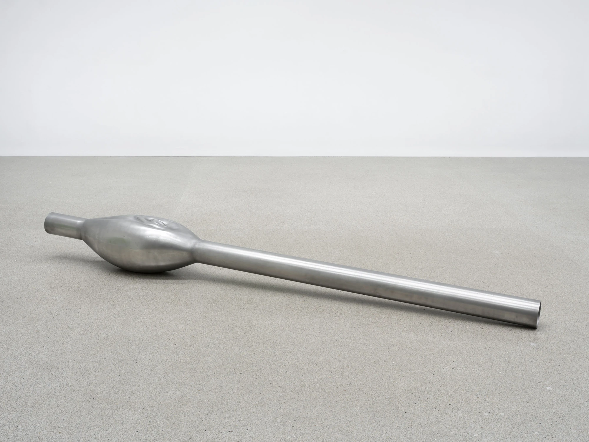 Dolls' Theater by Mimosa Echard, photographed by Julien Gremaud, Annik Wetter — A brushed steel straw lies on grey concrete, its shaft tapering away from a swollen bulb at one end.