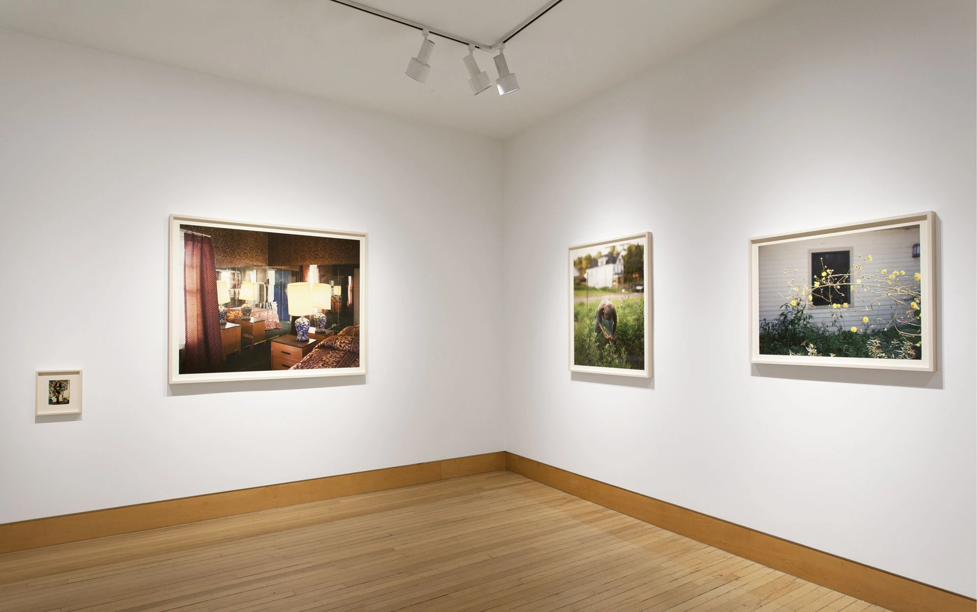 Installation view of a gallery corner, a large interior photograph on the left wall and three smaller framed prints turning the corner to the right.