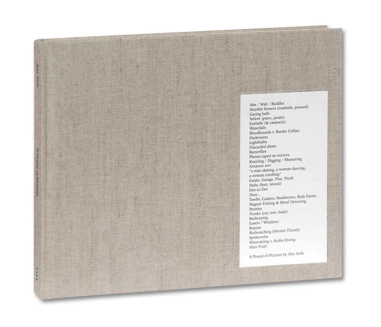 The book A Pound of Pictures, bound in oatmeal linen with a white label listing the subjects the pictures were made from, standing upright against a white ground.