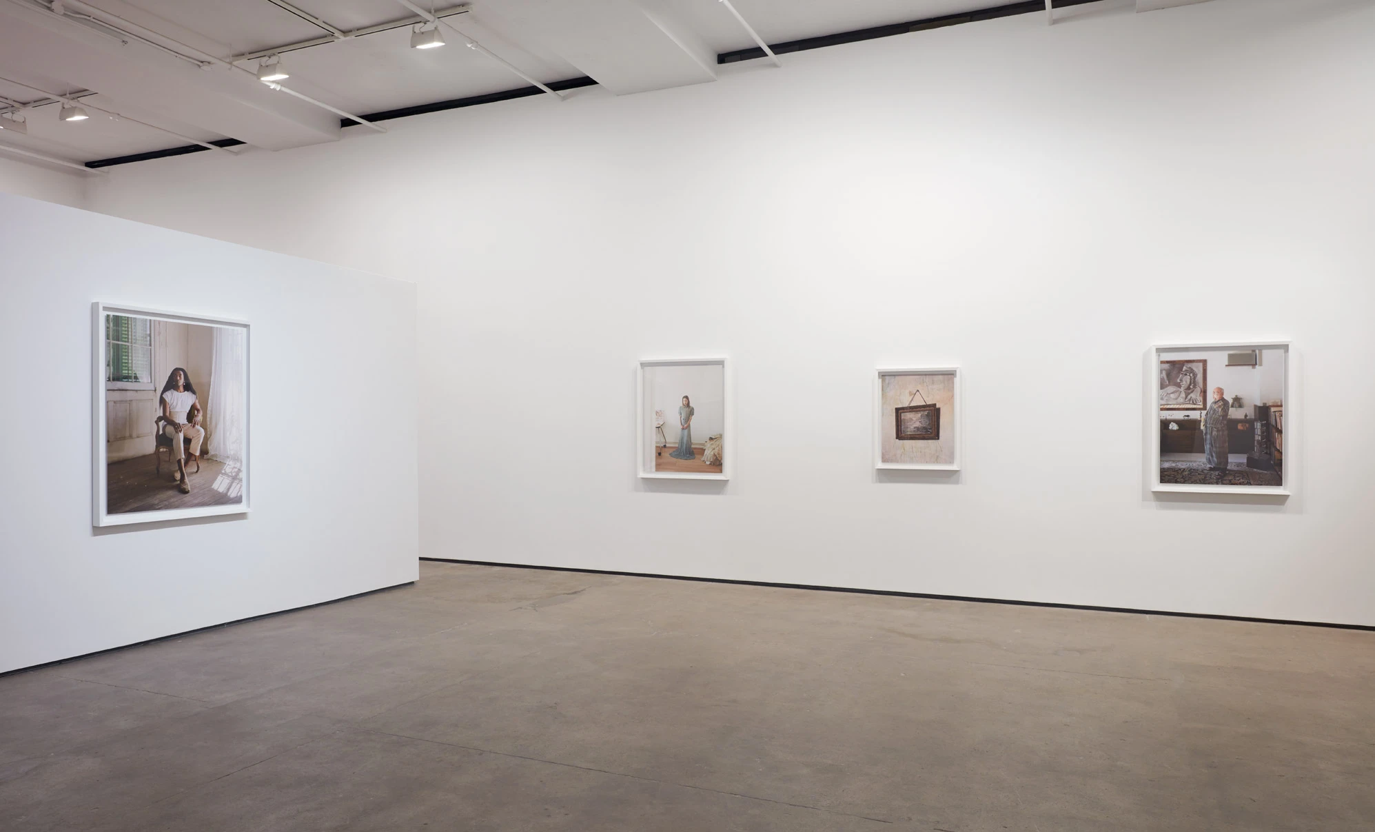 Installation view of the far wall, a large seated portrait at the left and three smaller framed prints spaced along the white wall to the right.