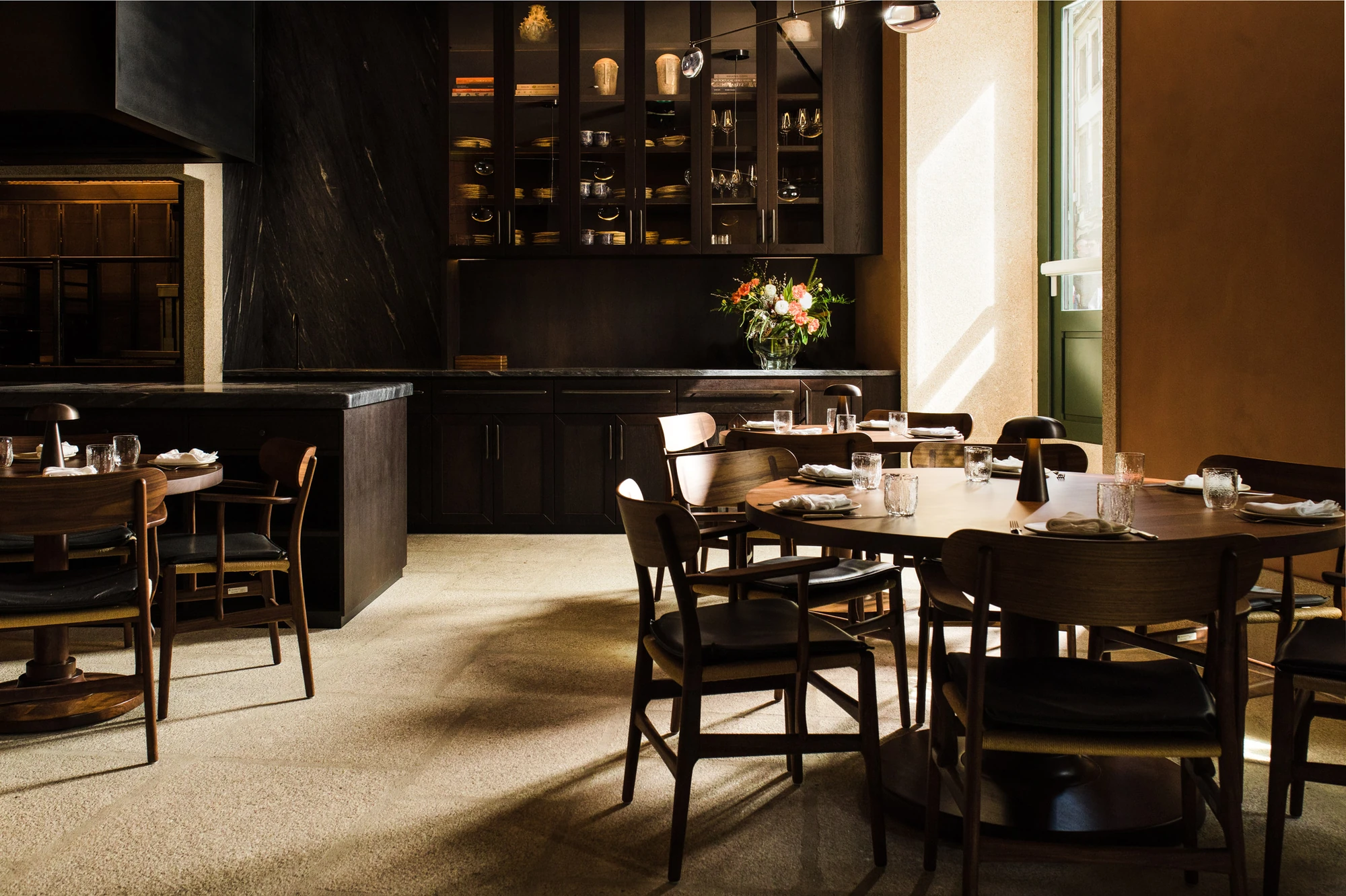 Cozinha das Flores Mural by Álvaro Siza, photographed by Luís Moreira — Late daylight crossing the pale aggregate floor of Cozinha das Flores toward the quartzite service counter and dark-stained cabinets.