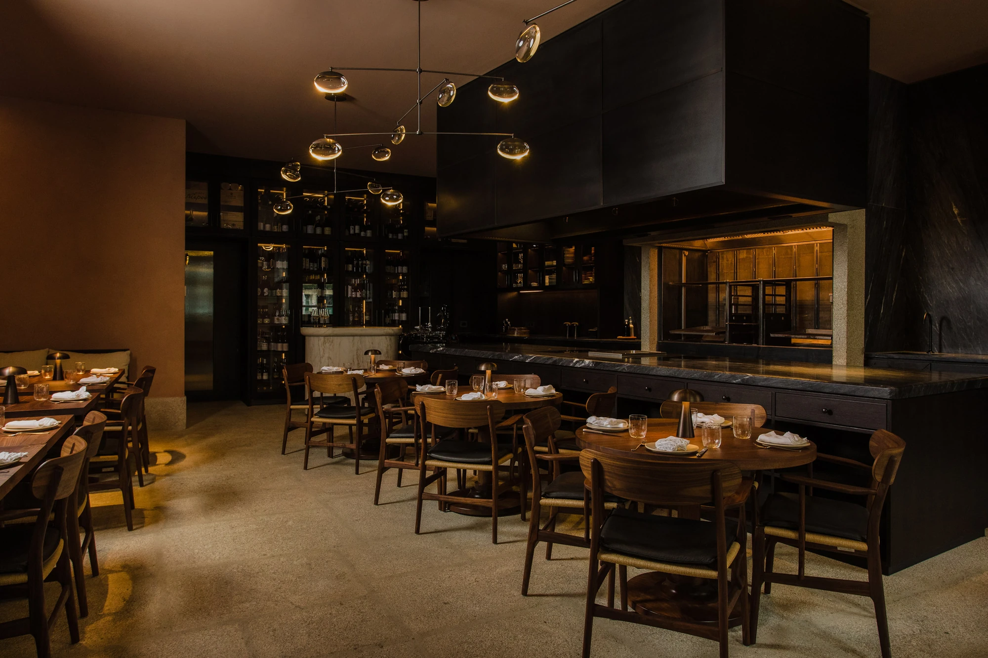 Cozinha das Flores Mural by Álvaro Siza, photographed by Luís Moreira — Dining room at Cozinha das Flores with dark wood tables, a jointed mobile light fixture overhead and glazed cabinets of Portuguese wine along the back wall.